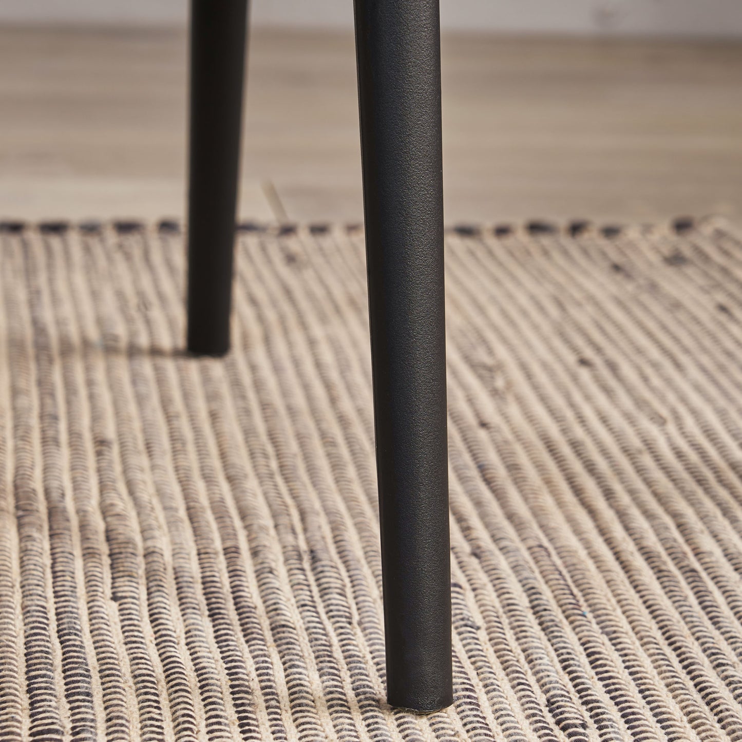 Black metal table leg with textured finish on woven rug