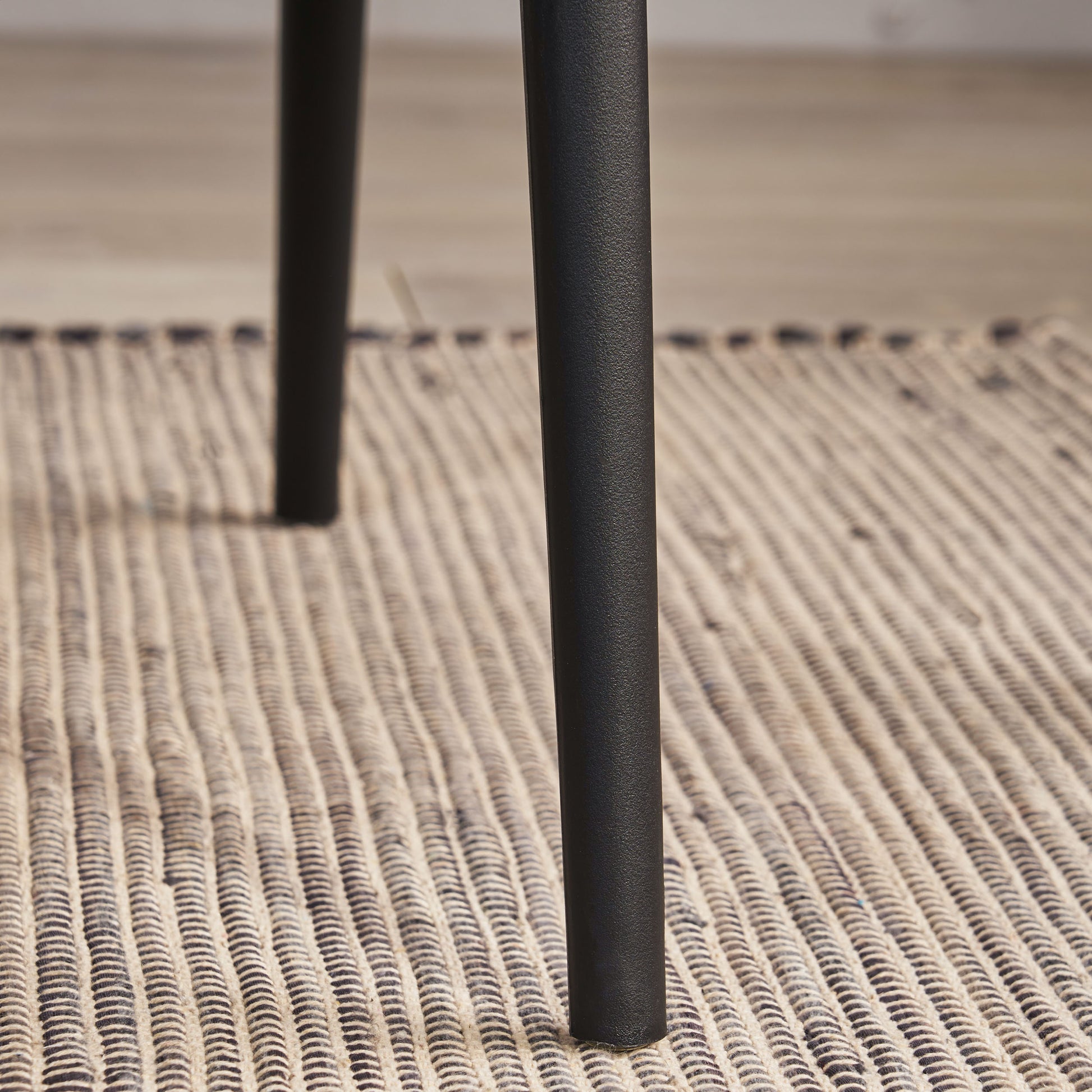 Black metal table leg with textured finish on woven rug