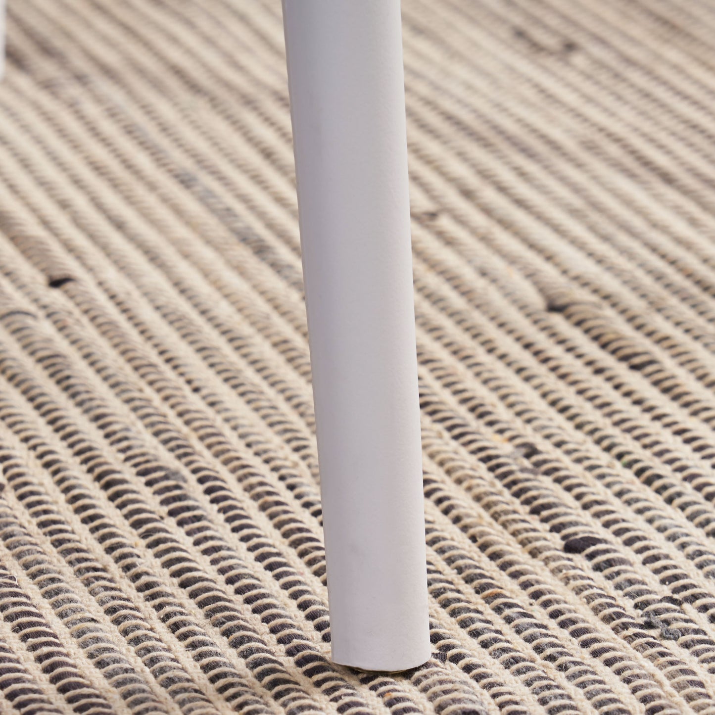 Closeup of a white chair leg on a textured rug