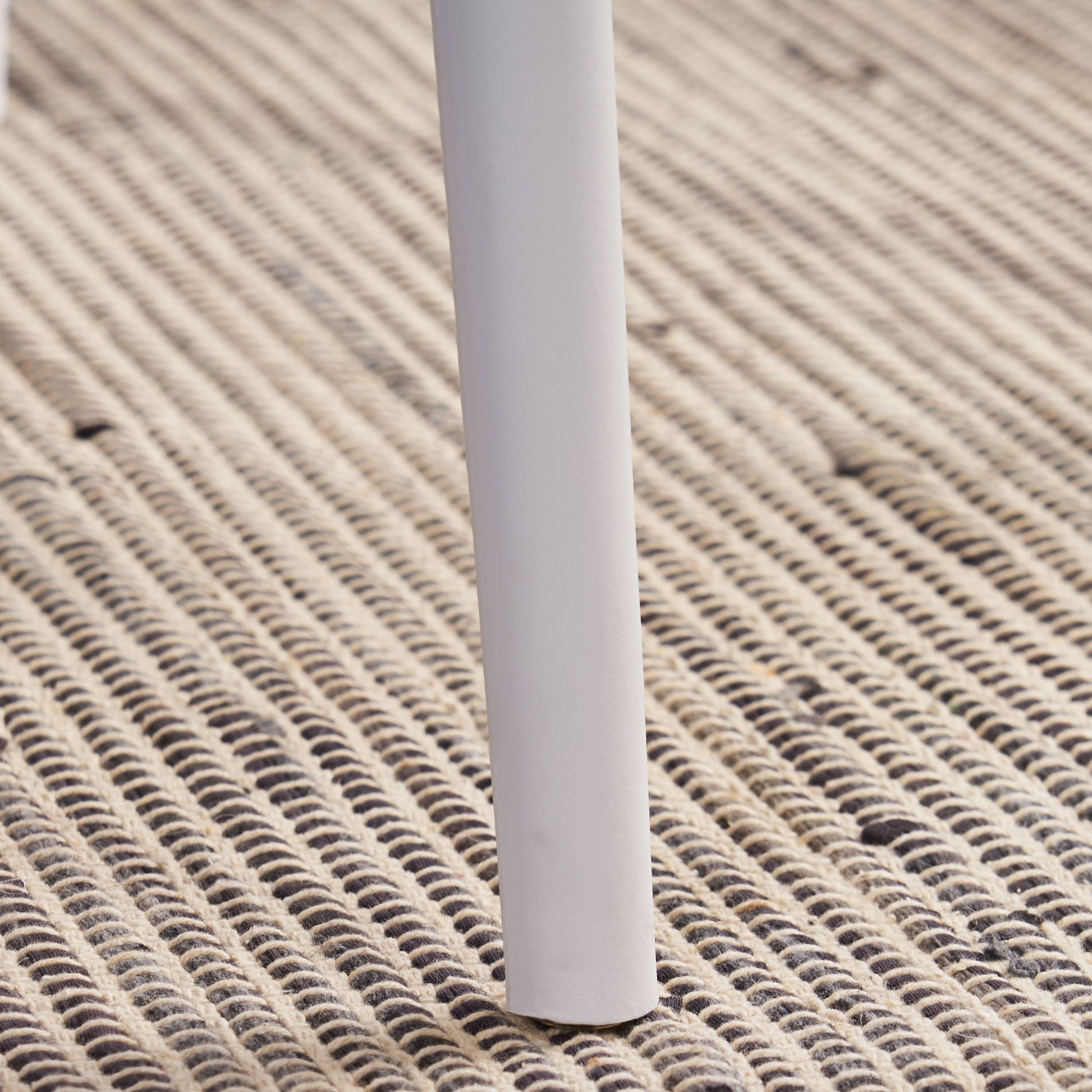 Closeup of a white chair leg on a textured rug