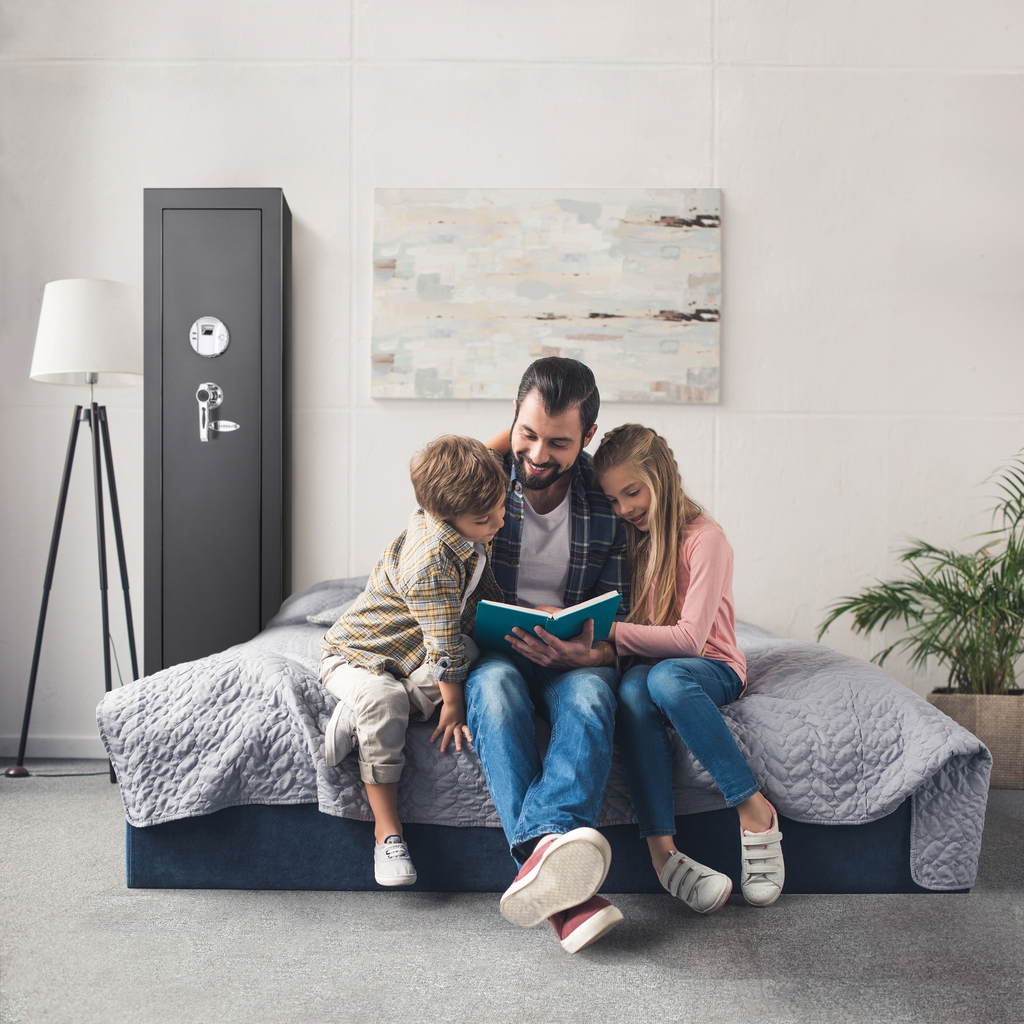 Father reading book to son and daughter on bed next to gun safe