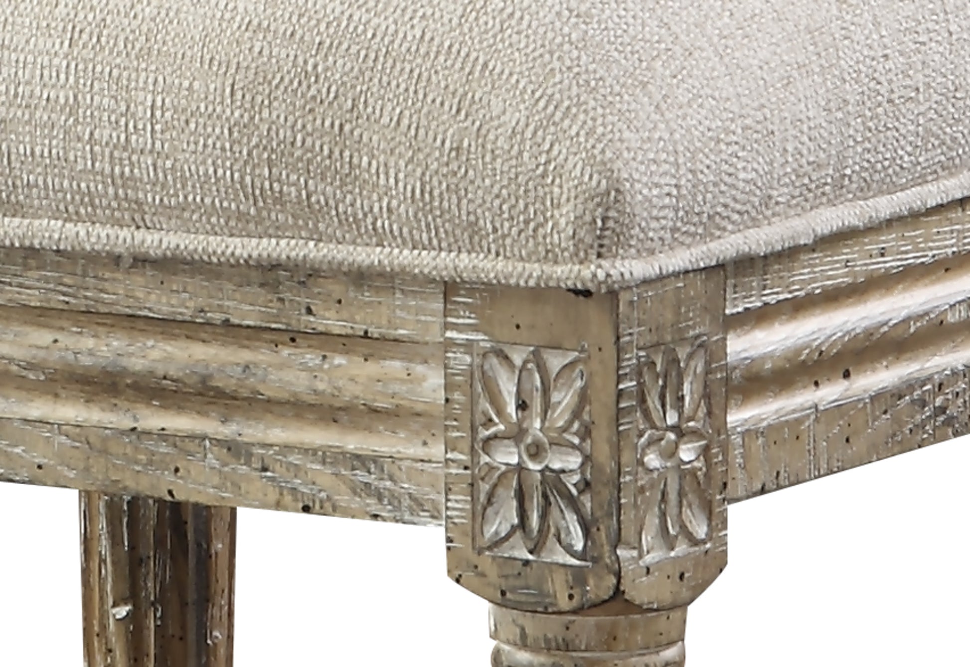 Closeup of a light beige upholstered ottoman with carved wooden legs