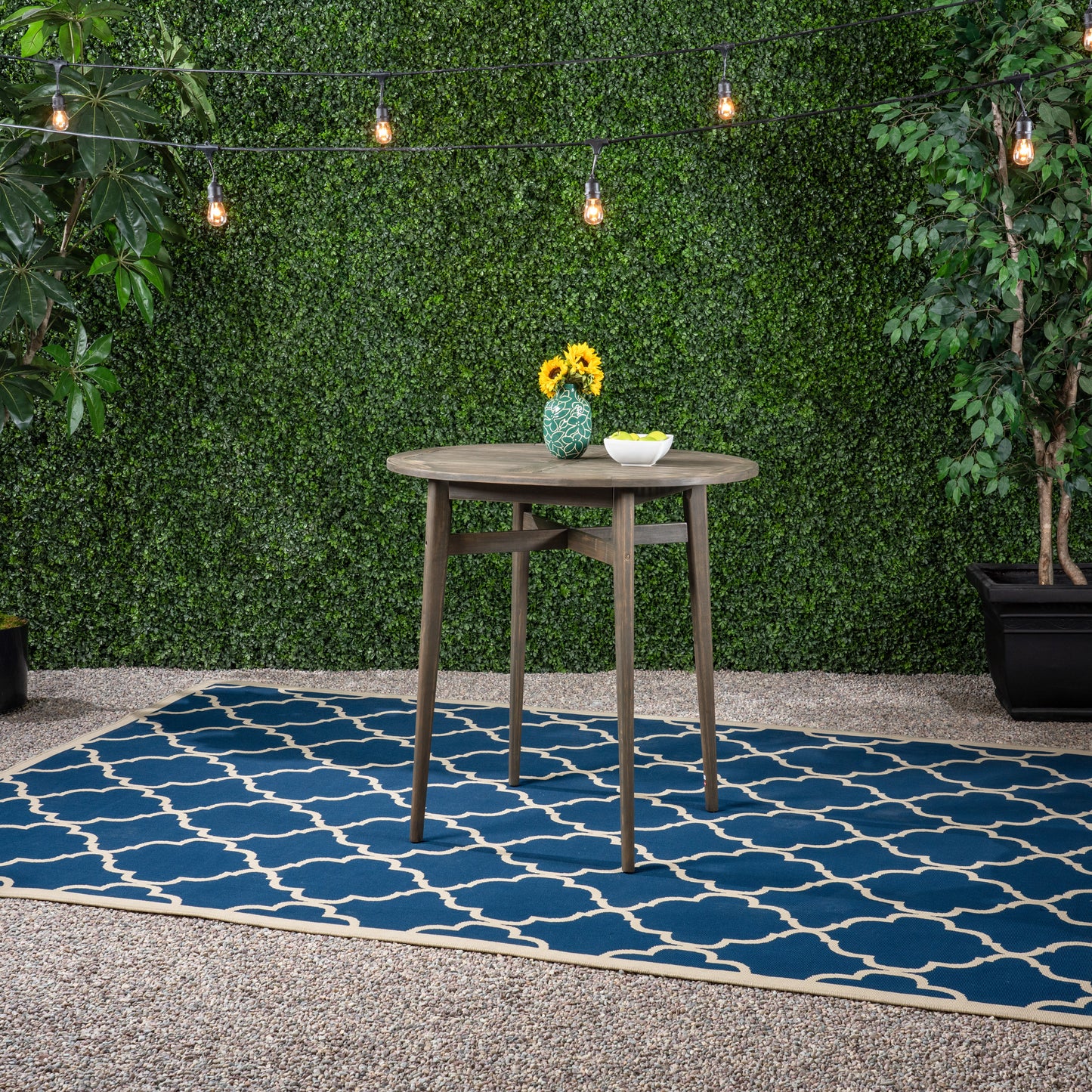 Dark wood round patio table with sunflowers in green vase on blue Moroccan trellis rug