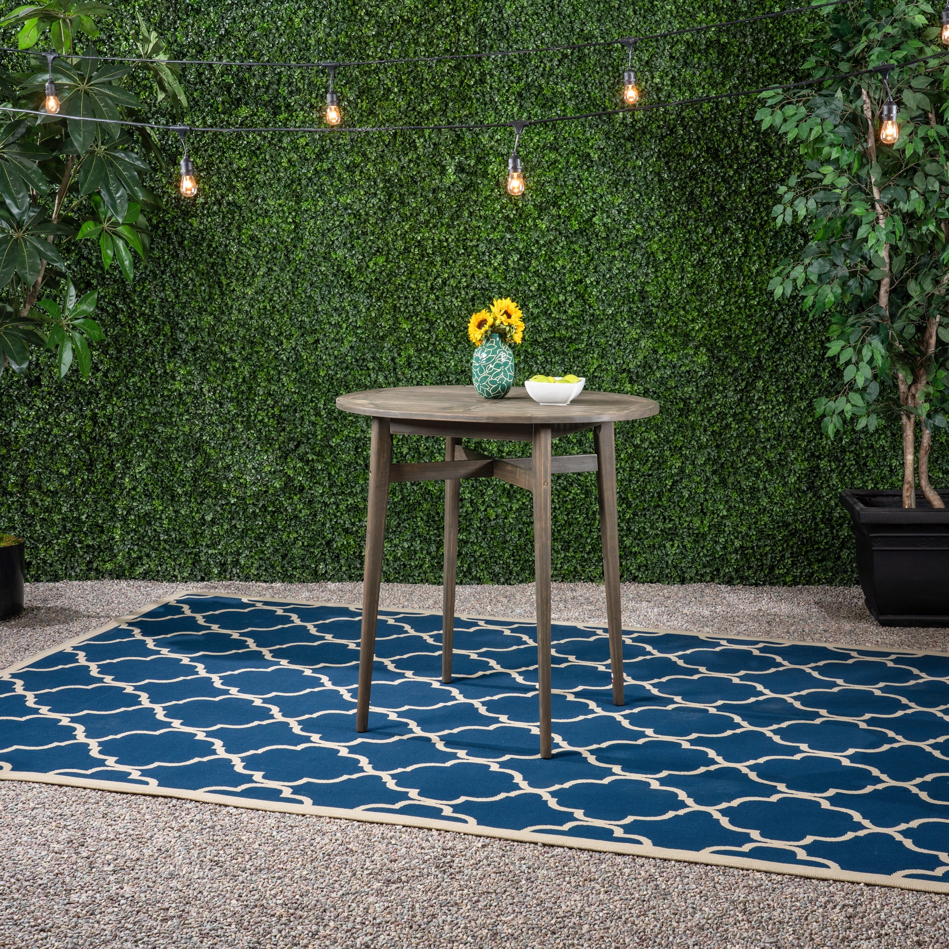 Dark wood round patio table with sunflowers in green vase on blue Moroccan trellis rug