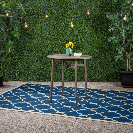 Dark wood round patio table with sunflowers in green vase on blue Moroccan trellis rug