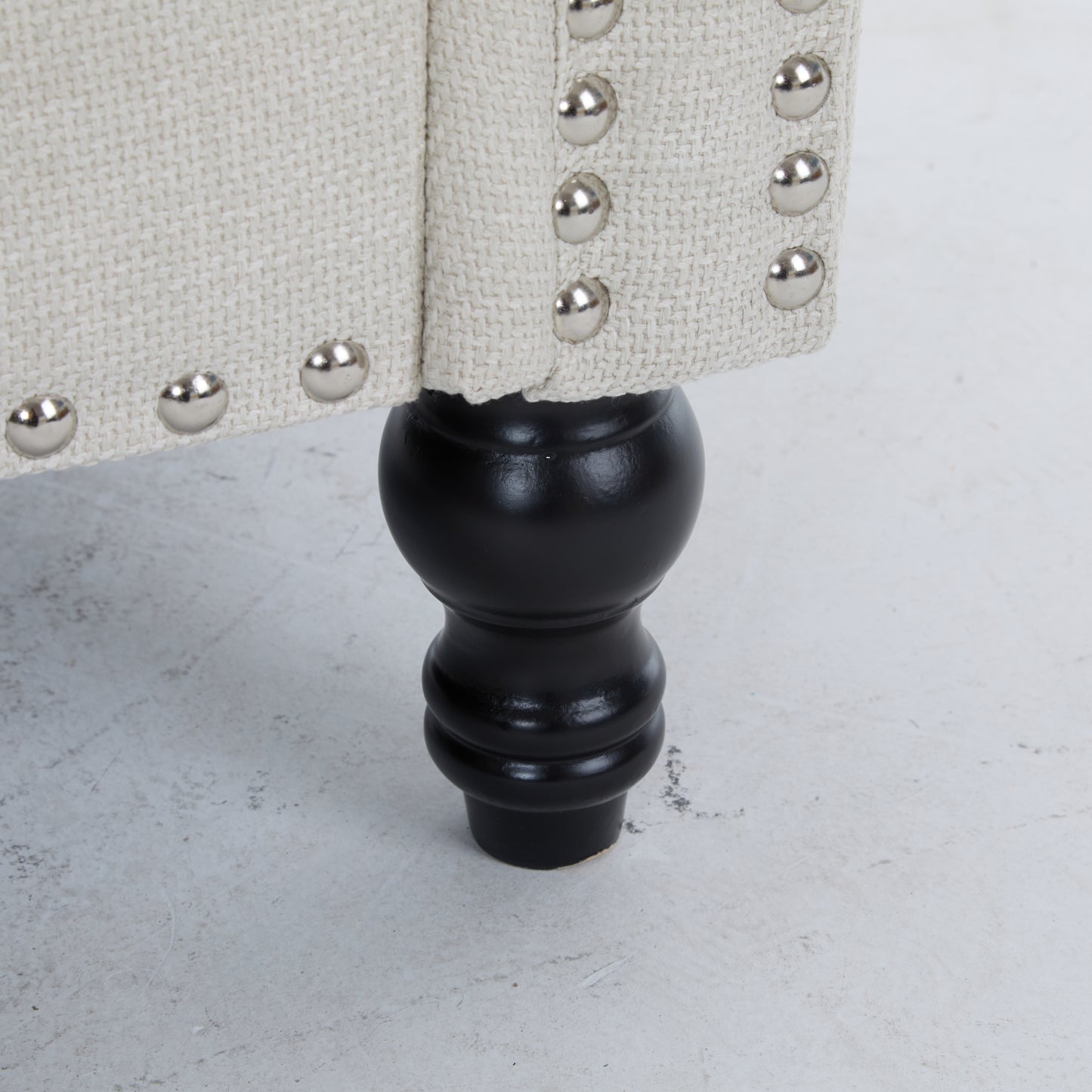 Beige linen upholstered armchair detail with silver nailhead trim and black turned leg