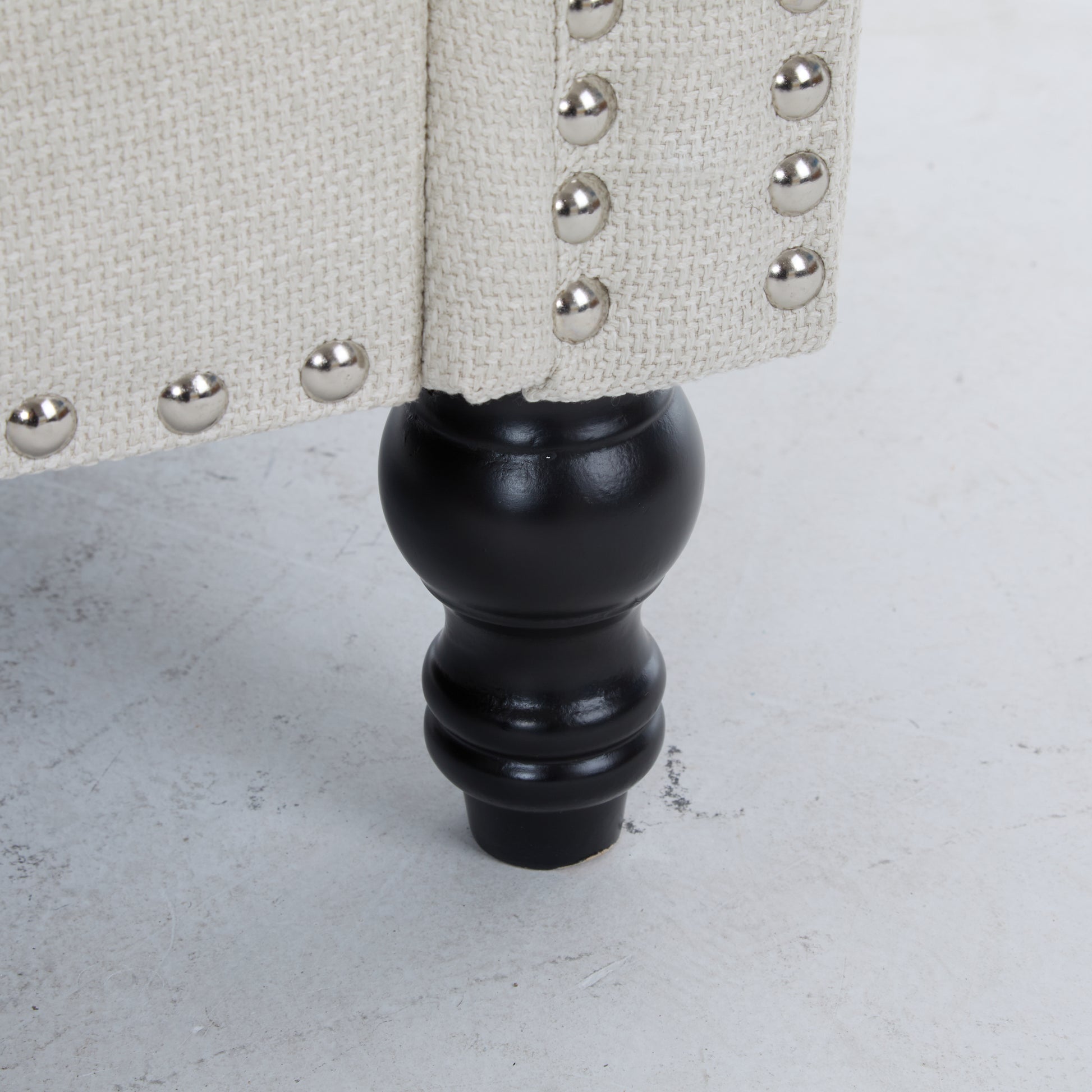 Beige linen upholstered armchair detail with silver nailhead trim and black turned leg