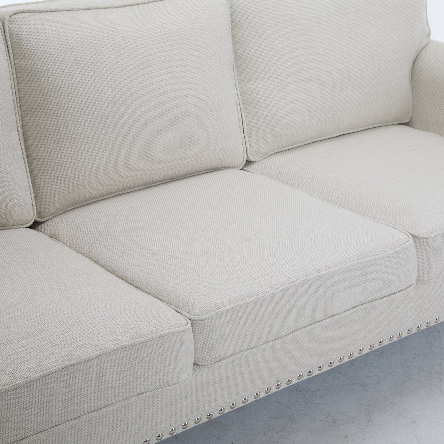 Closeup of a creamcolored upholstered sofa with silver nailhead trim