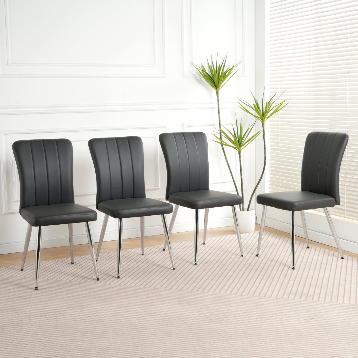 Four black faux leather dining chairs with vertical stitching and silver legs