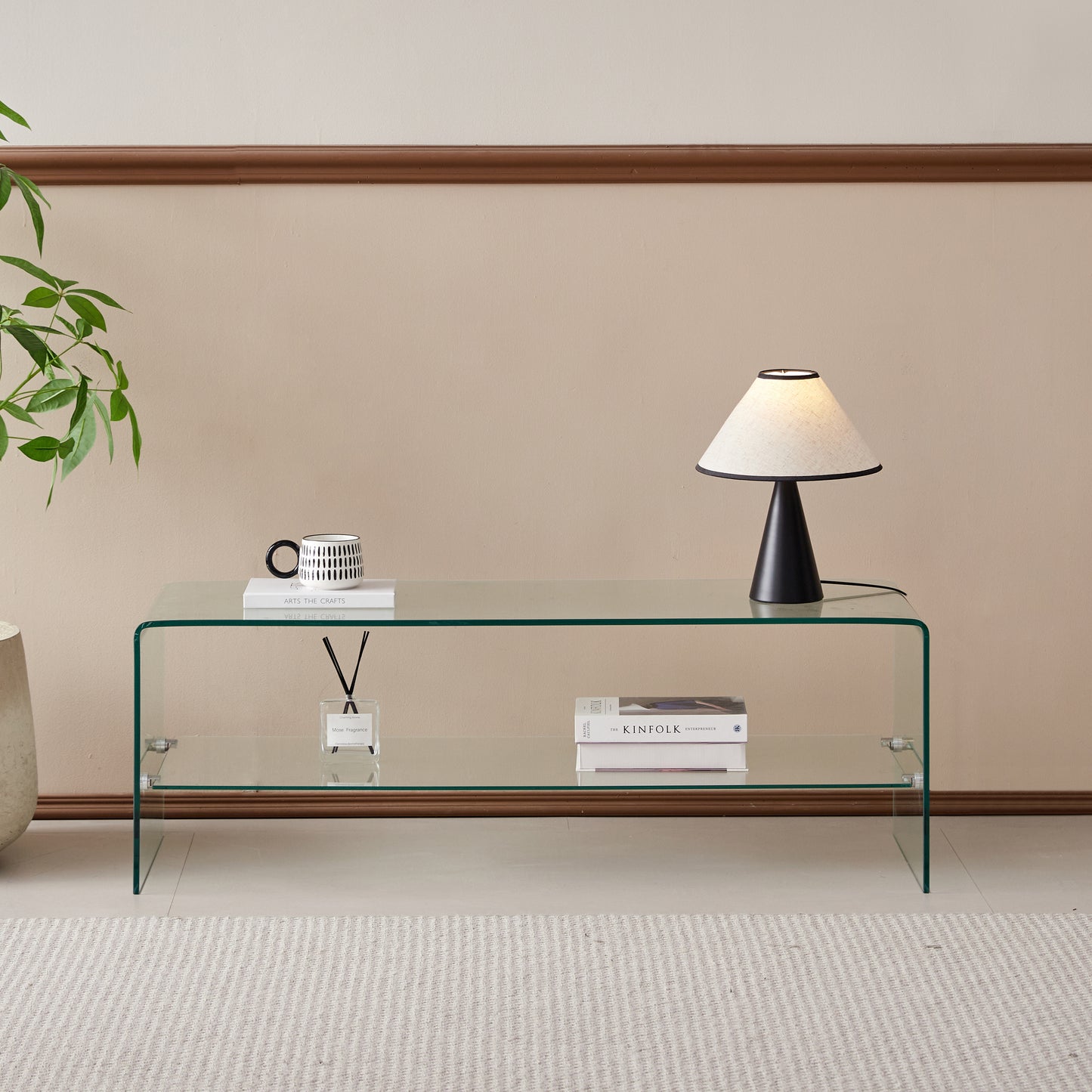 Clear glass coffee table with two shelves displaying books and a diffuser