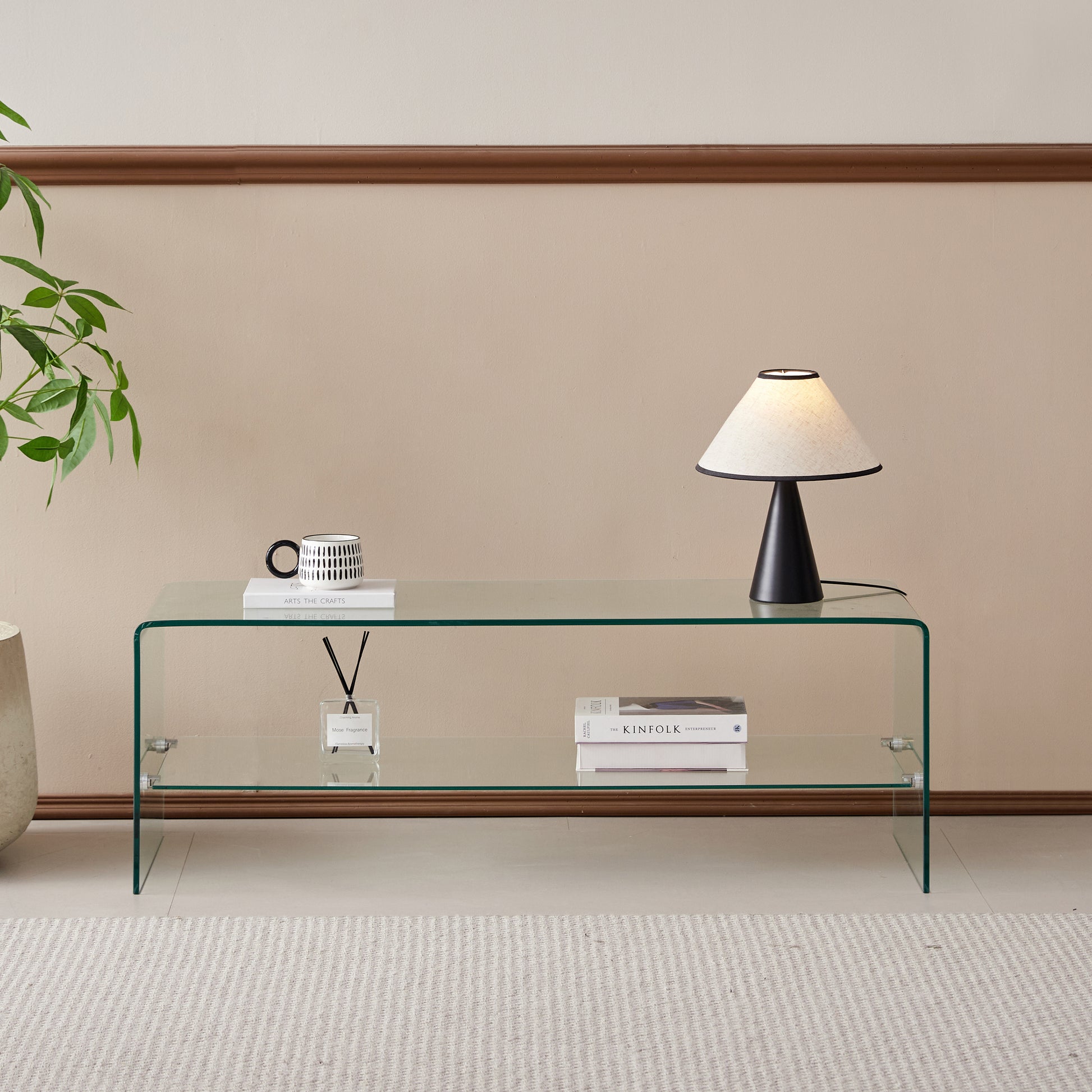 Clear glass coffee table with two shelves displaying books and a diffuser