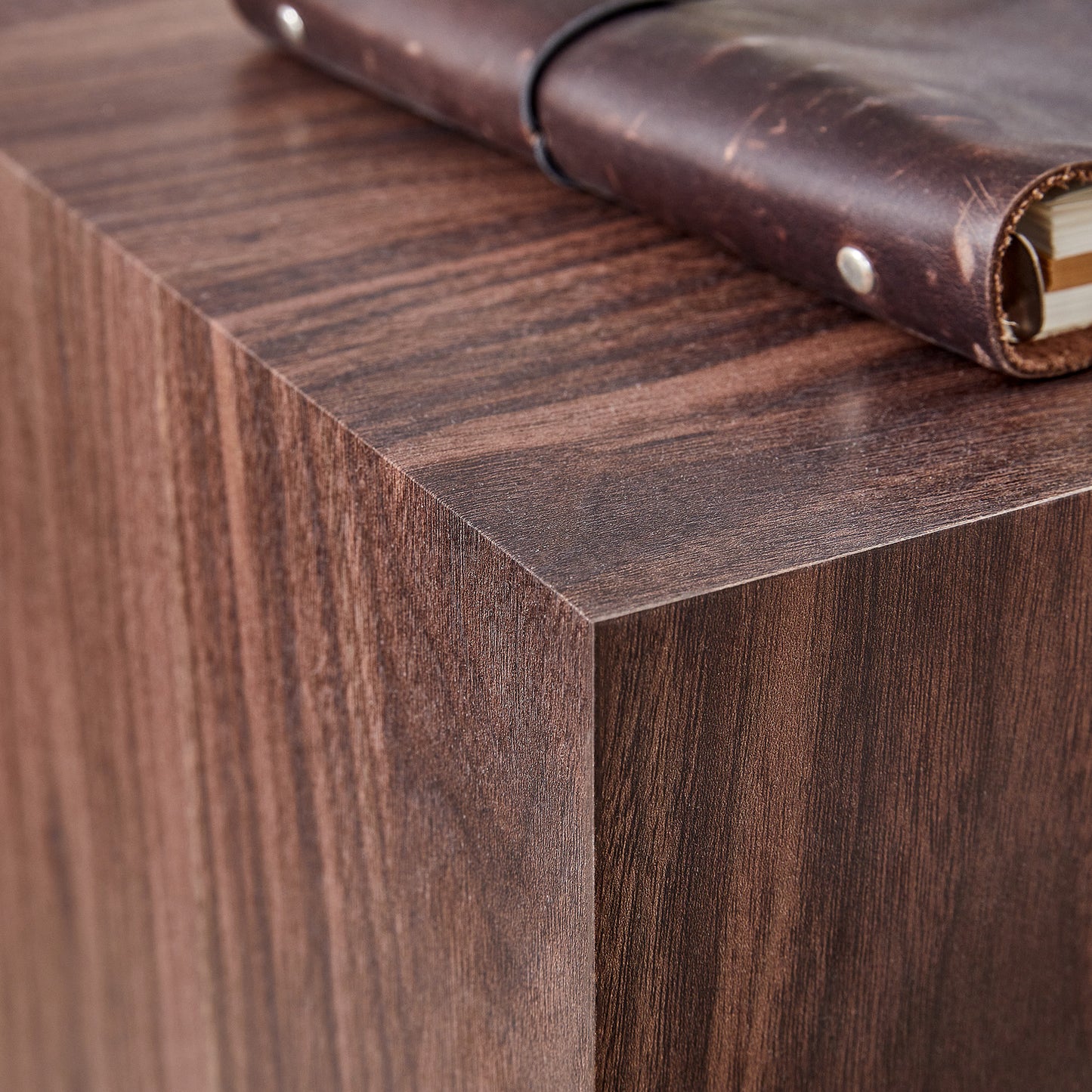 Dark brown faux wood side table with a leather journal on top