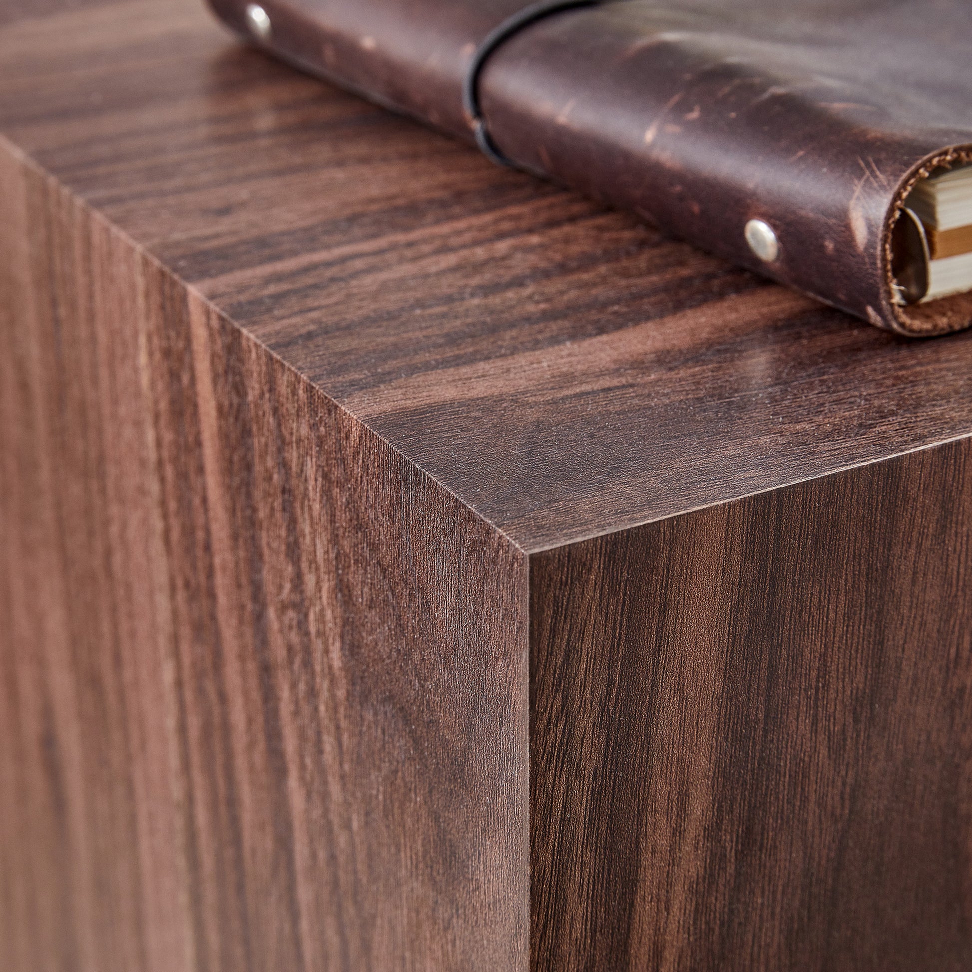 Dark brown faux wood side table with a leather journal on top