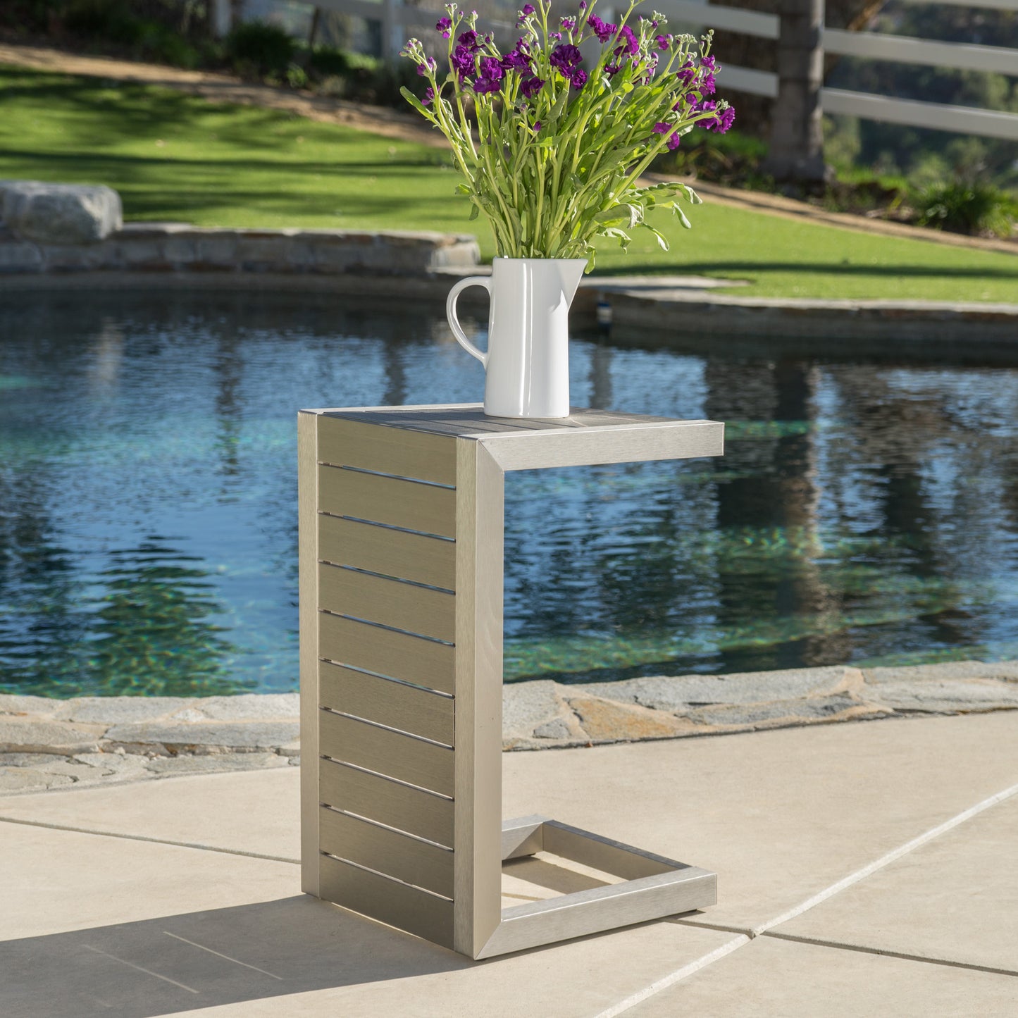 Modern ctable with silver frame and taupe slat design next to pool