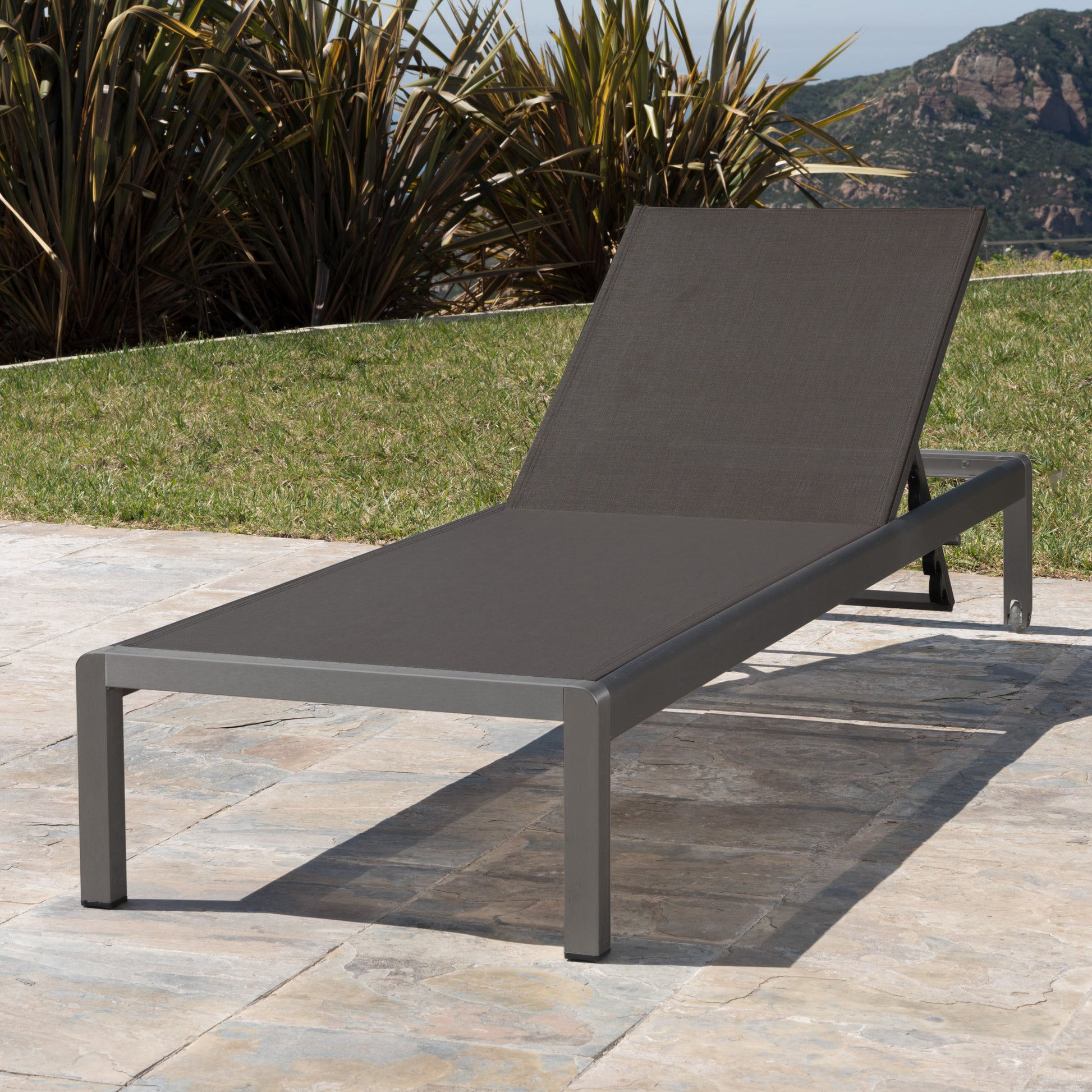 Charcoal grey outdoor chaise lounge with adjustable backrest on stone patio