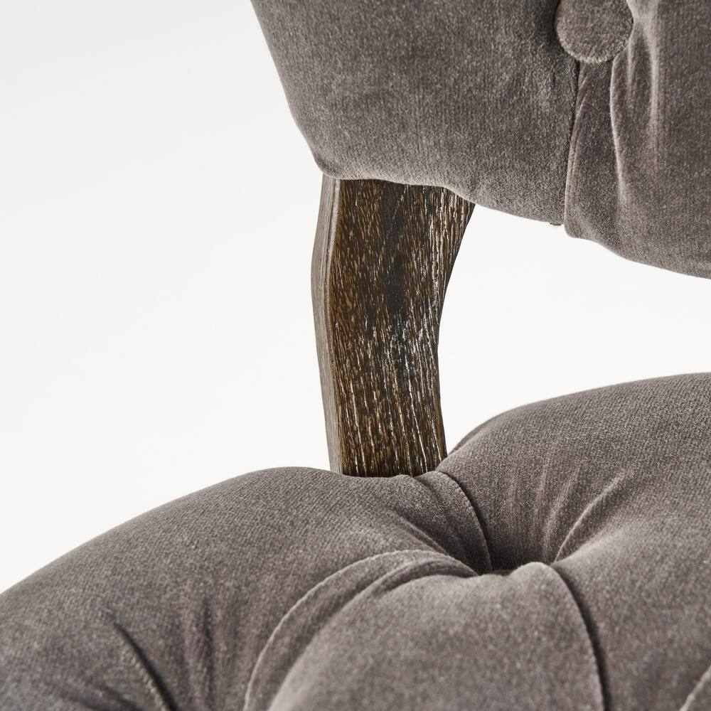 Closeup of tufted grey fabric armchair armrest with dark wood accent