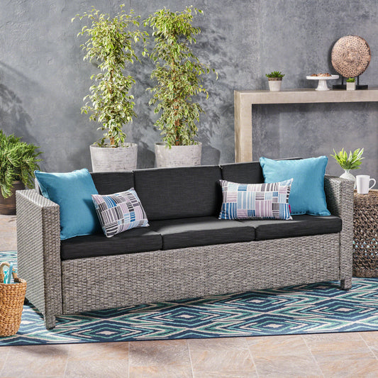 Gray rattan outdoor sofa with dark cushions and teal throw pillows