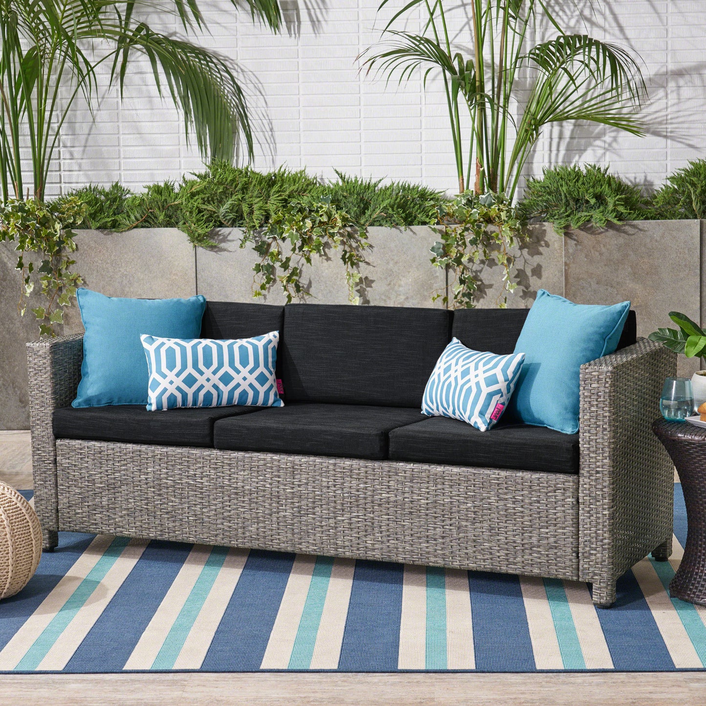 Gray wicker patio sofa with charcoal cushions and blue geometric pillows