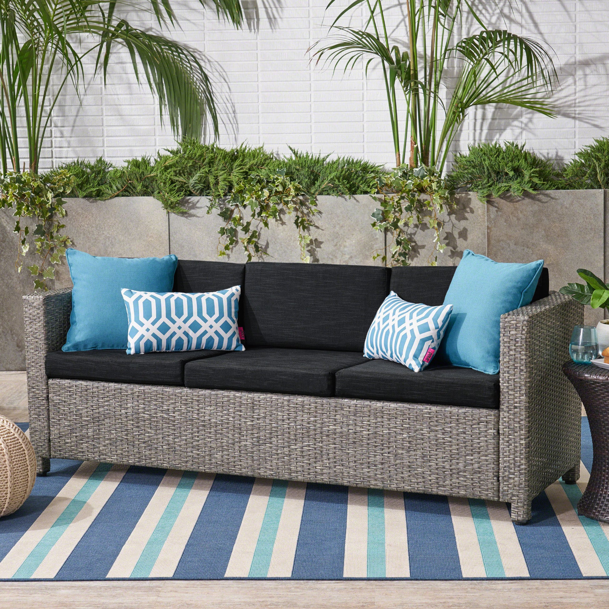 Gray wicker patio sofa with charcoal cushions and blue geometric pillows