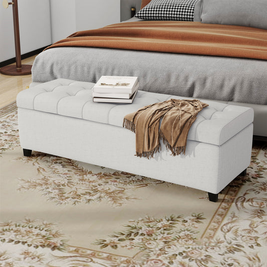 Light grey tufted storage ottoman with a brown throw blanket and books