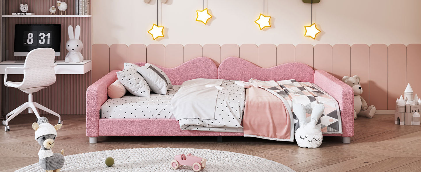 Pink boucl upholstered daybed with a wavy headboard and playful bedding