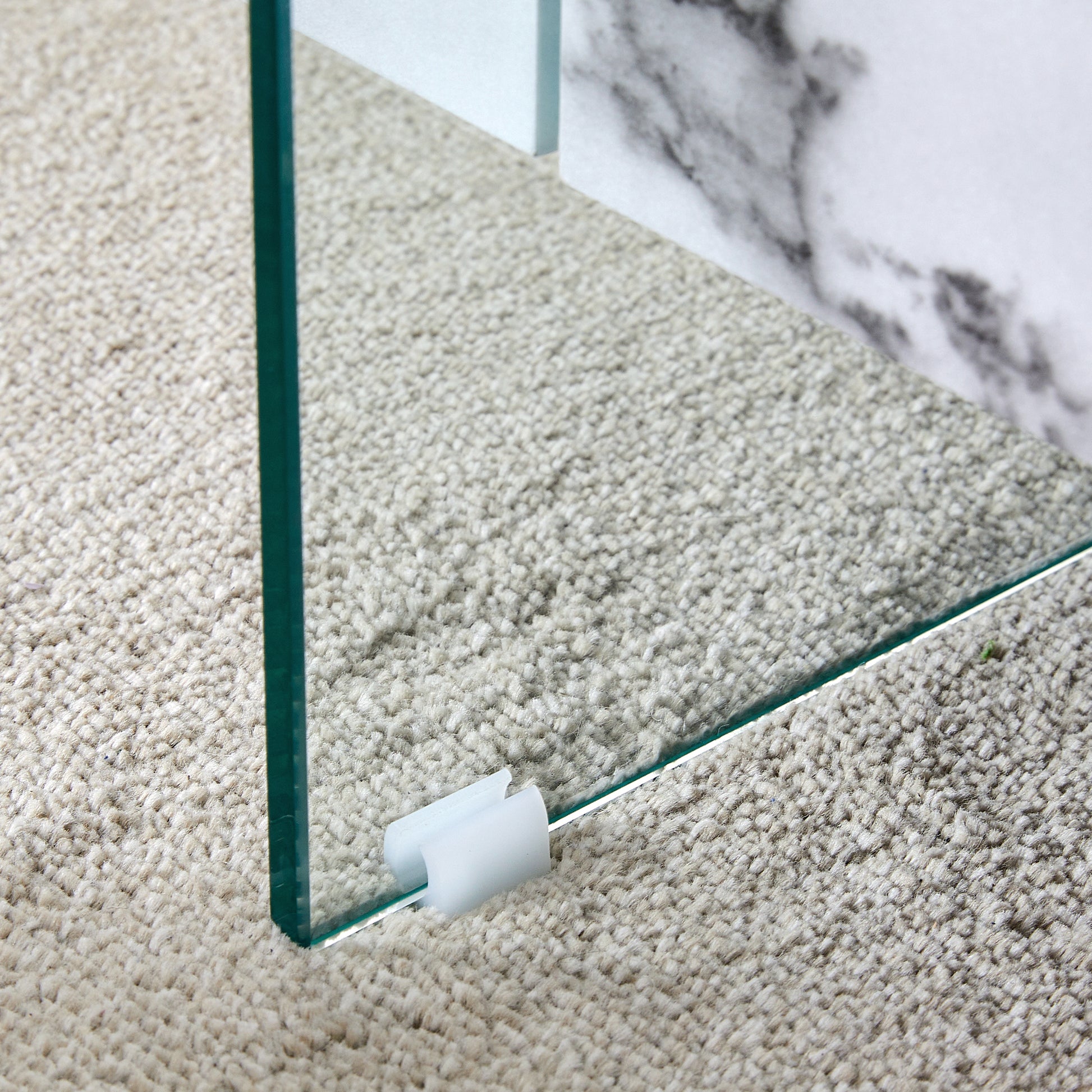 Clear glass shelf edge with white clip on textured beige carpet