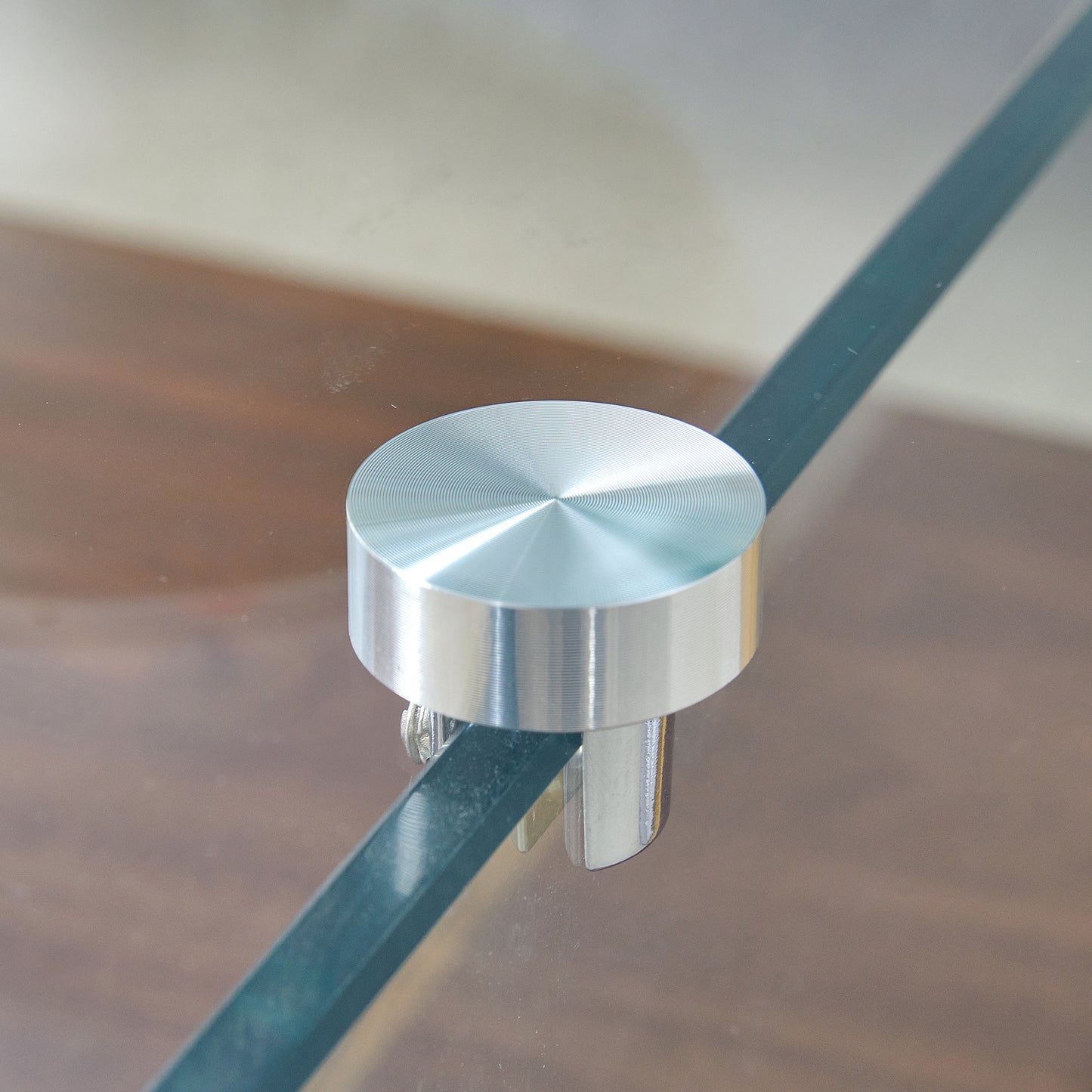 Brushed aluminum standoff with concentric circles detail on glass shelf