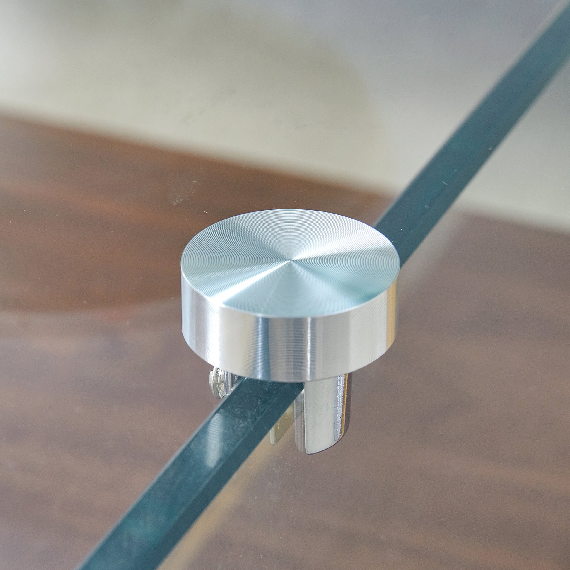 Brushed aluminum standoff with concentric circles detail on glass shelf