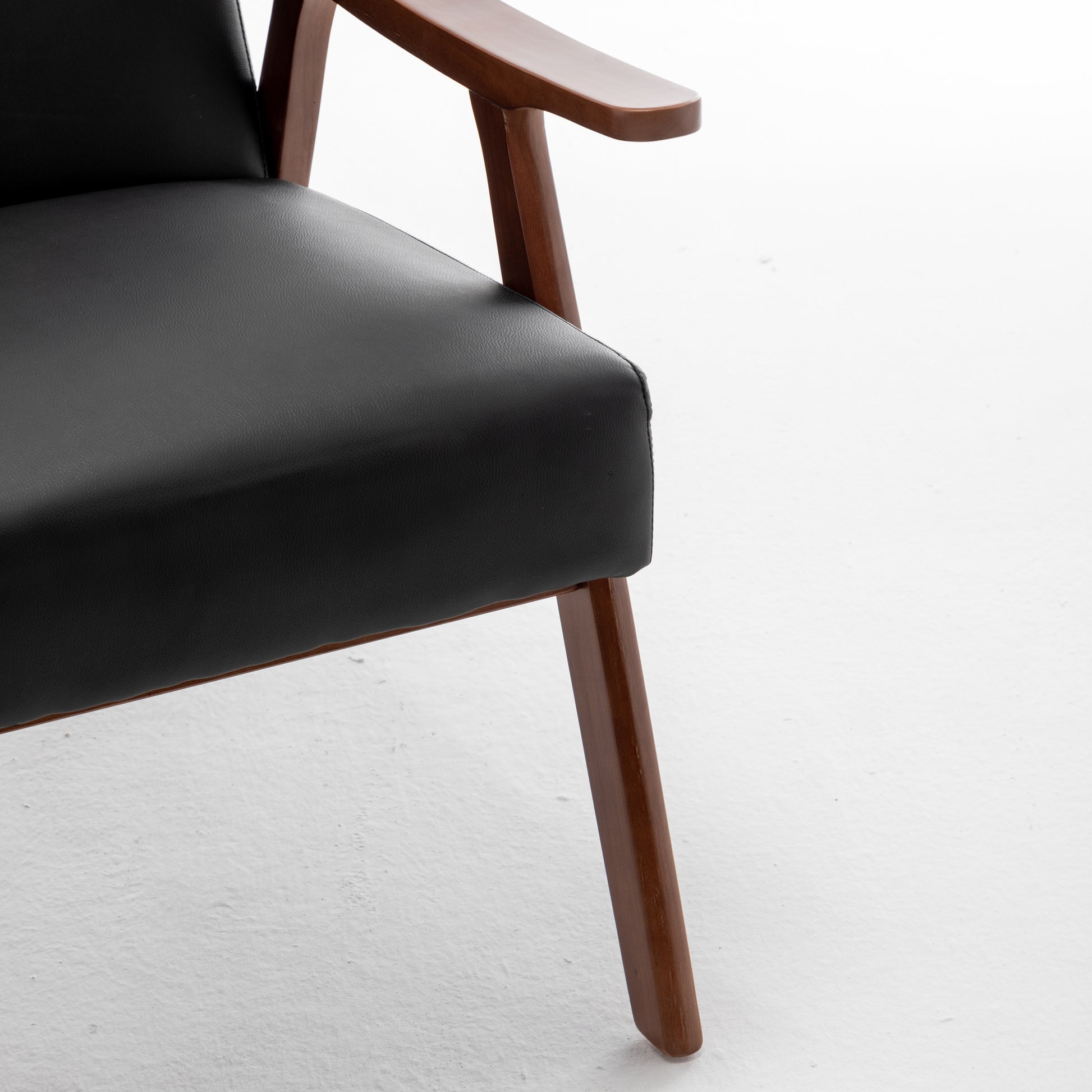 Black leather armchair with curved wooden armrest and tapered legs
