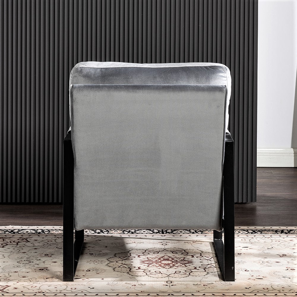 Back view of a plush grey velvet accent chair with black metal legs on a patterned rug