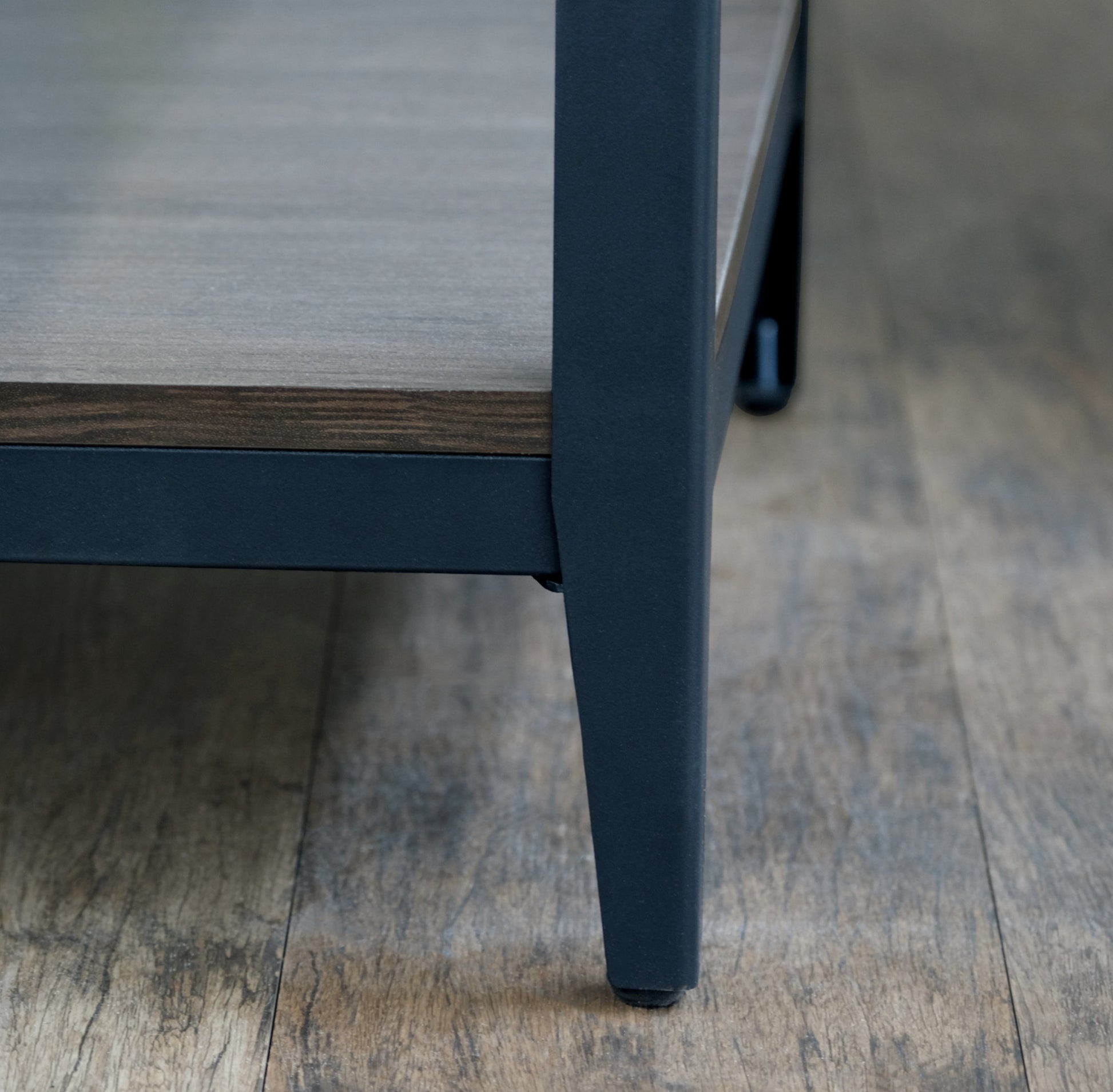 Closeup of a dark gray metal furniture leg supporting a woodeffect shelf
