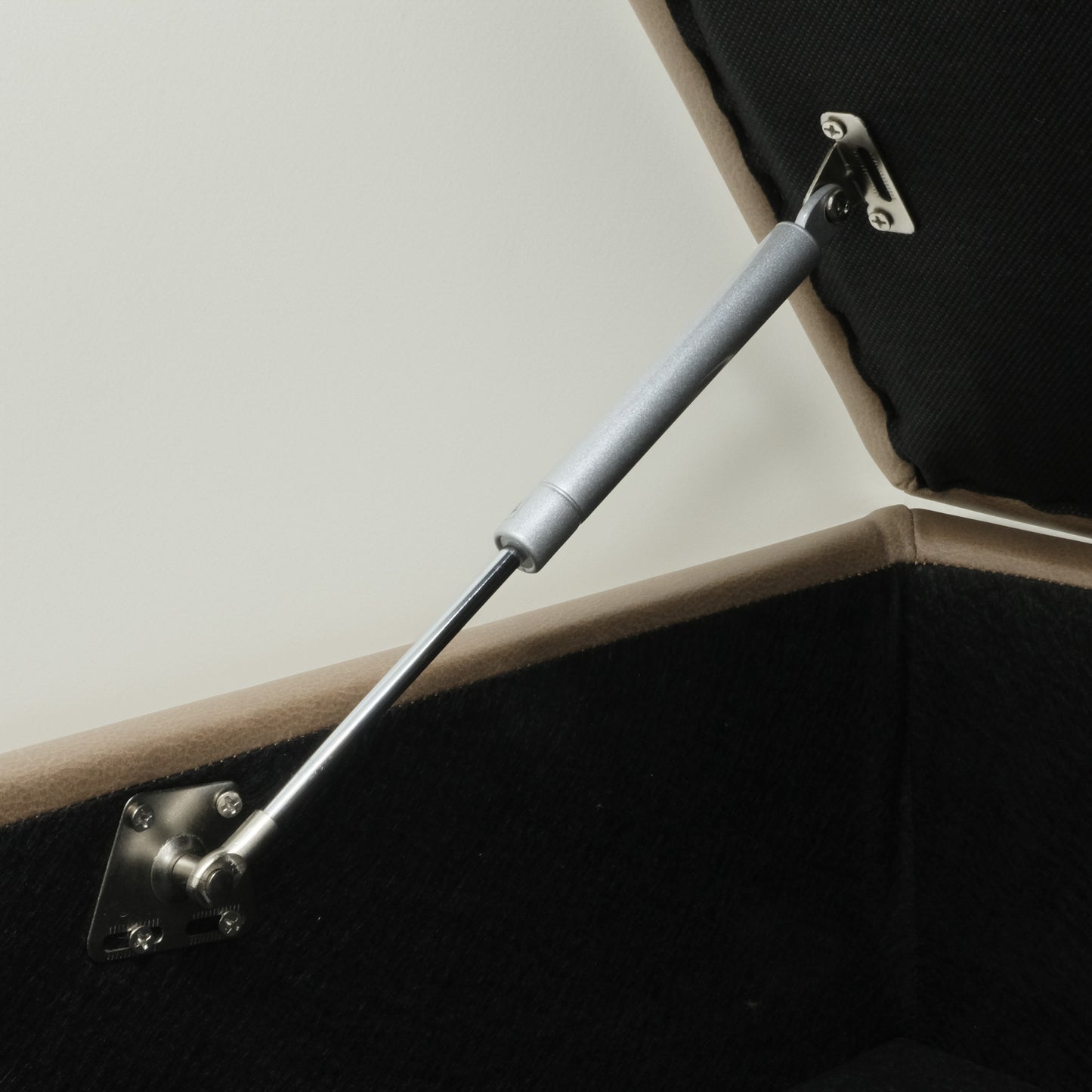 Metal gas strut on a tan fabric storage ottoman