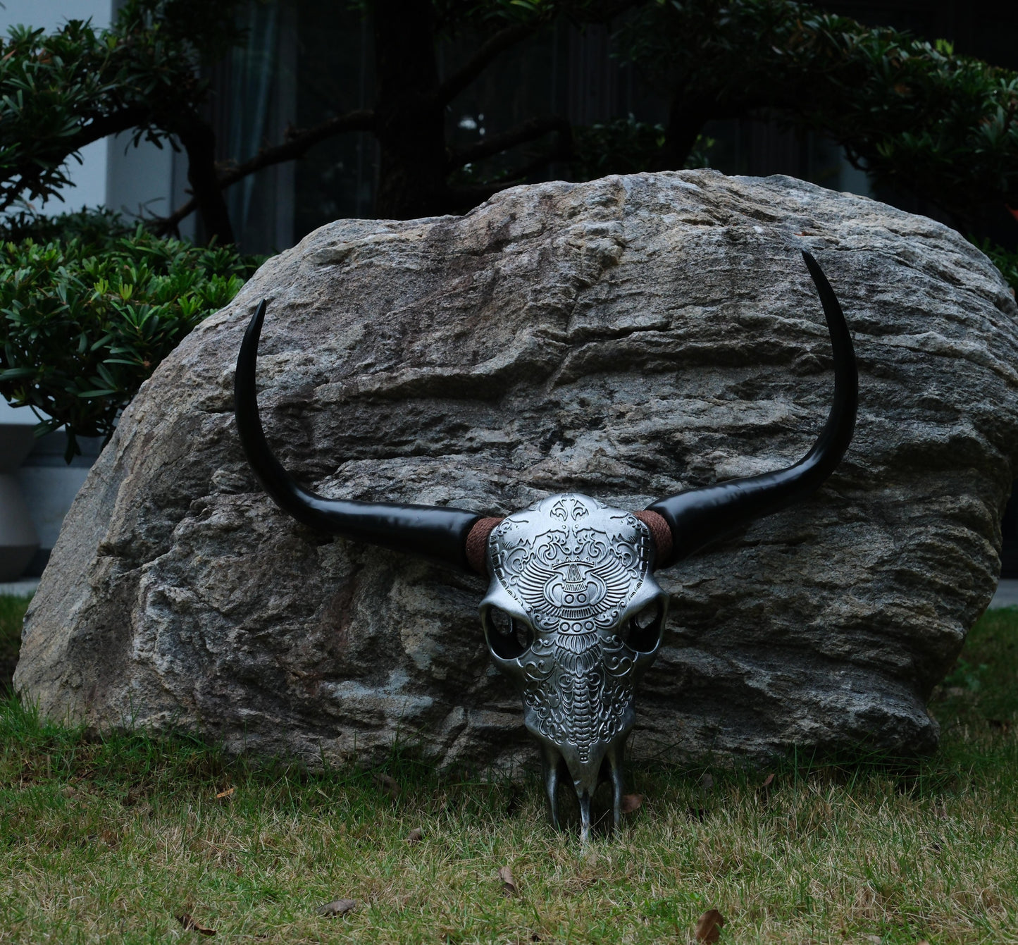 Ornate silver bull skull with large black horns displayed outdoors