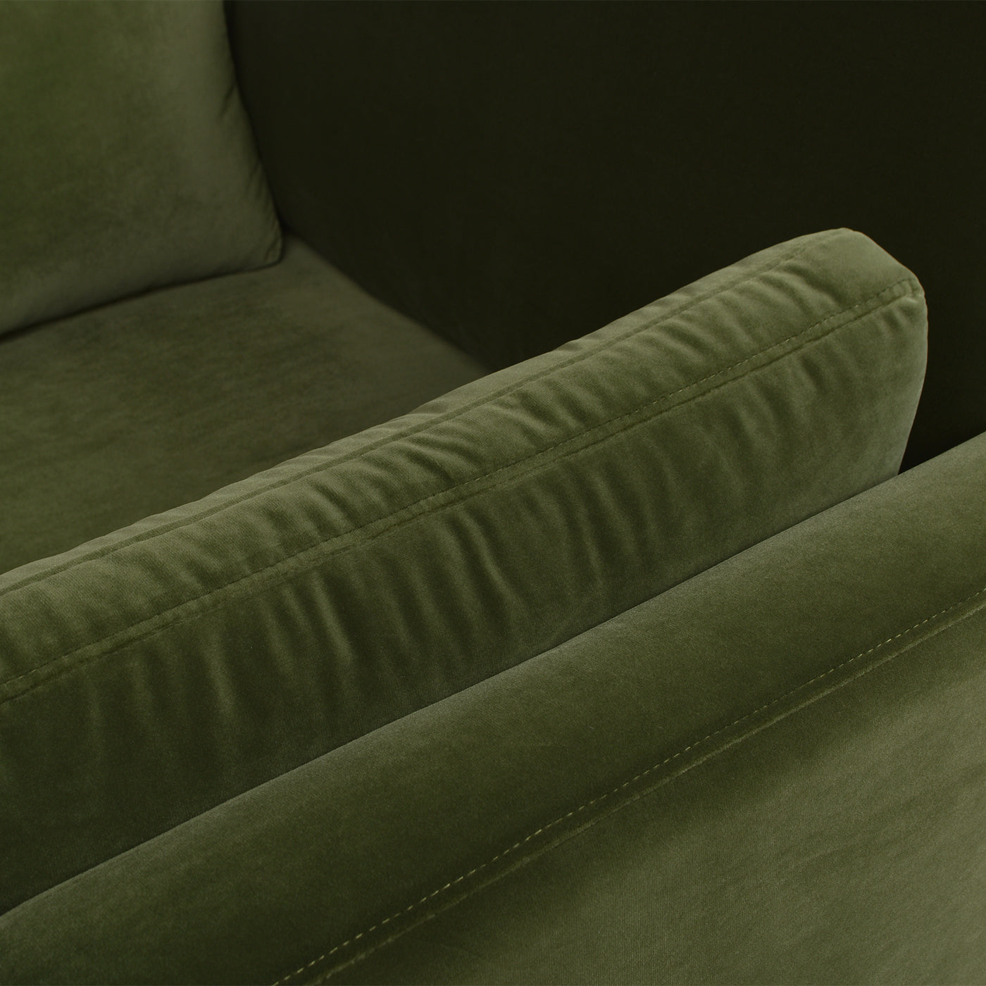 Closeup of plush olive green velvet armchair armrest with subtle stitching detail