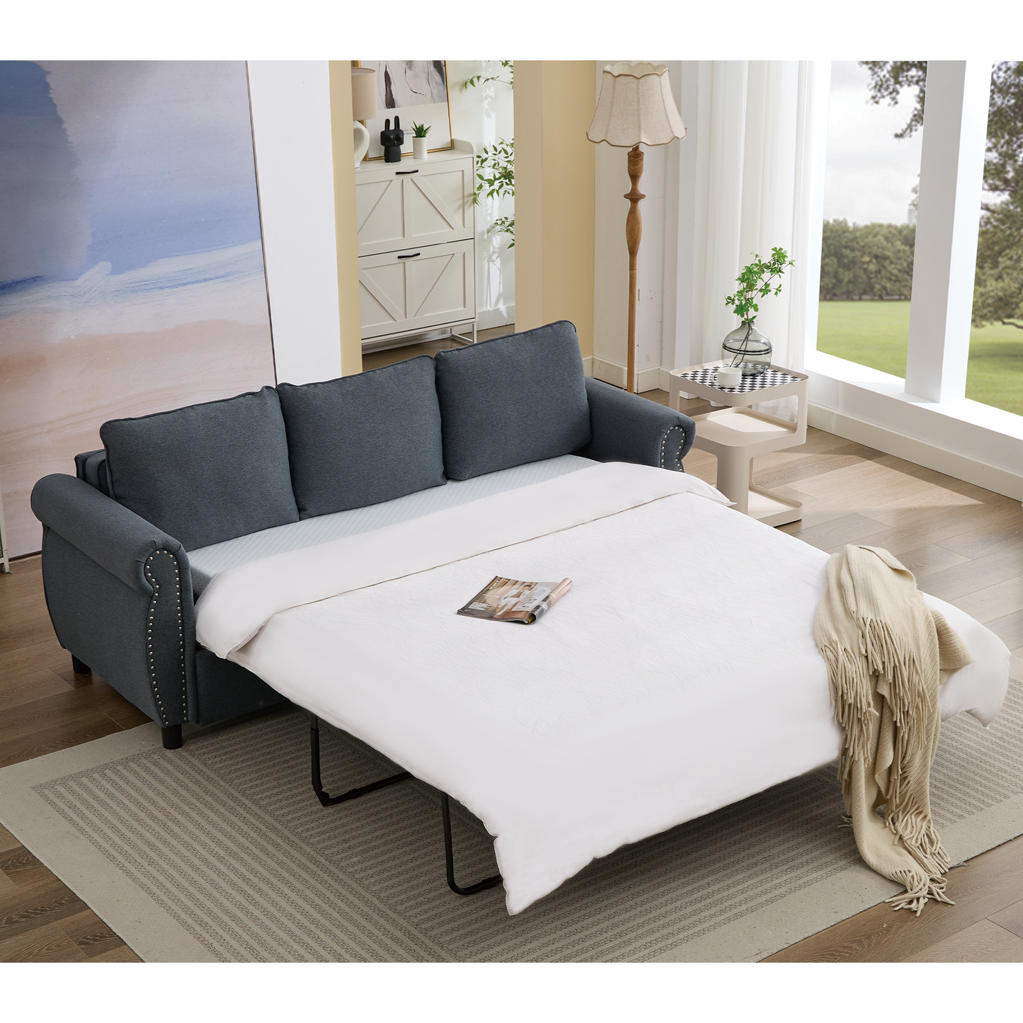 Dark gray upholstered sofa bed with silver stud accents and a cream fringed throw