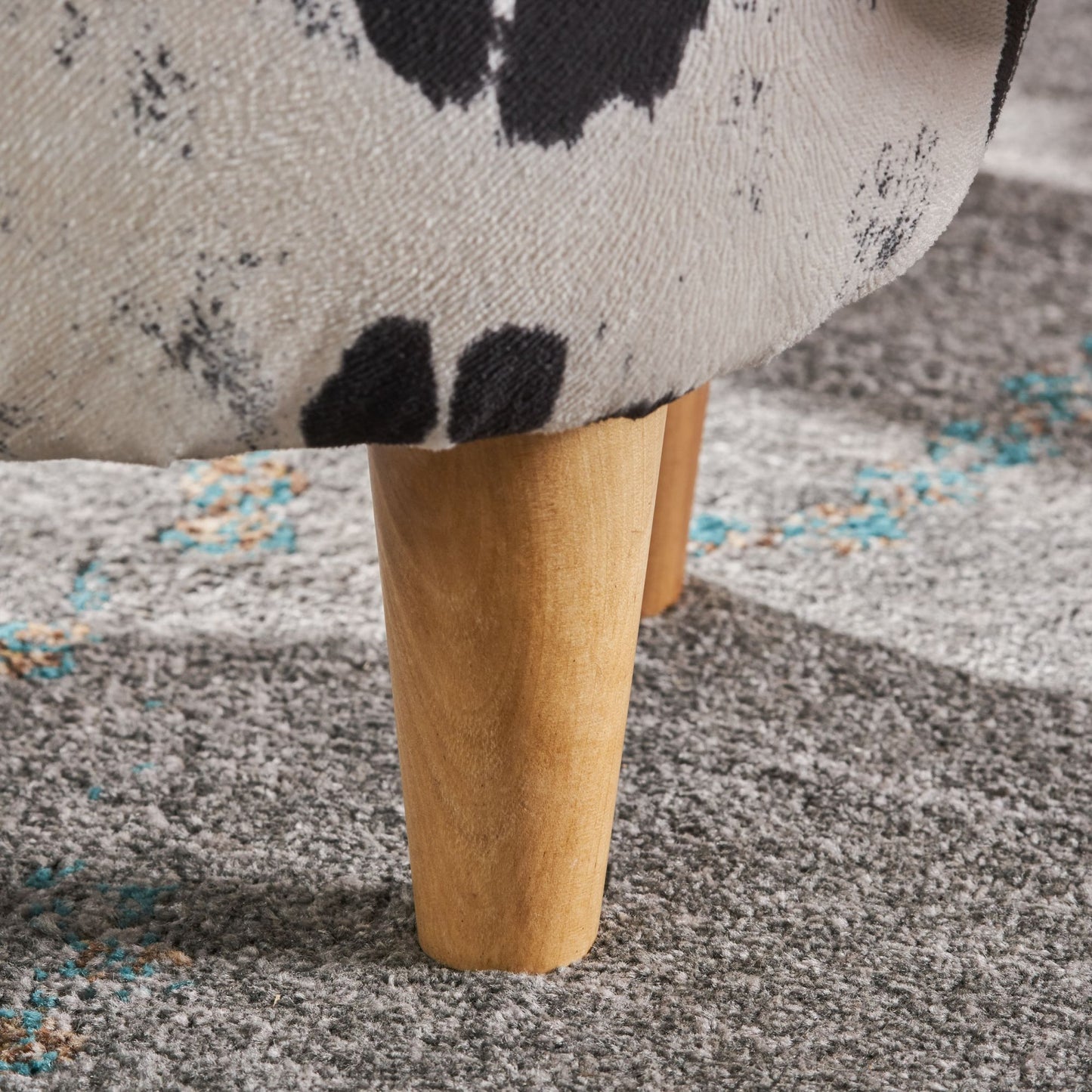Closeup of beige fabric with black abstract print and wooden leg on textured grey rug