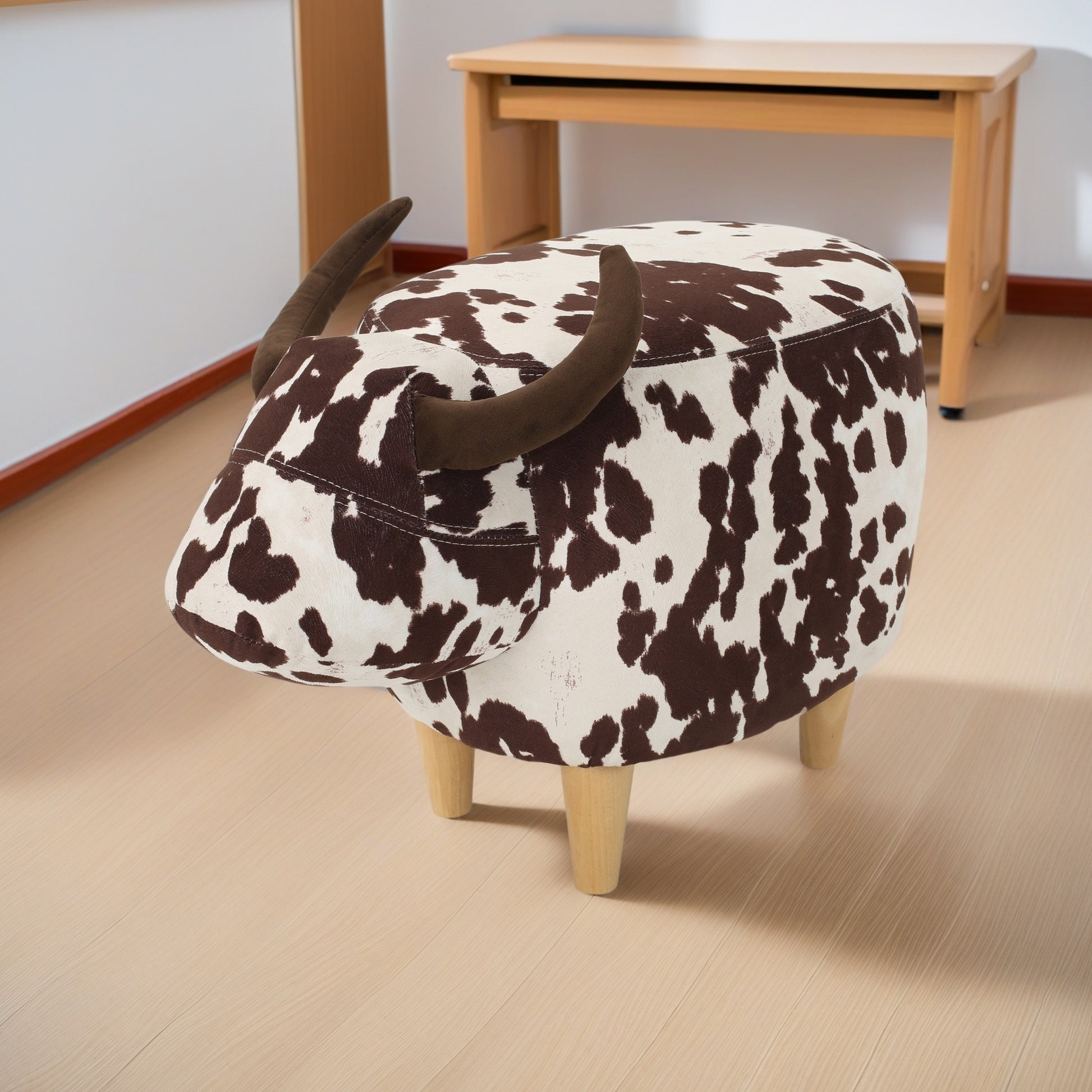 Whimsical cow print upholstered ottoman with faux horn details and wooden legs