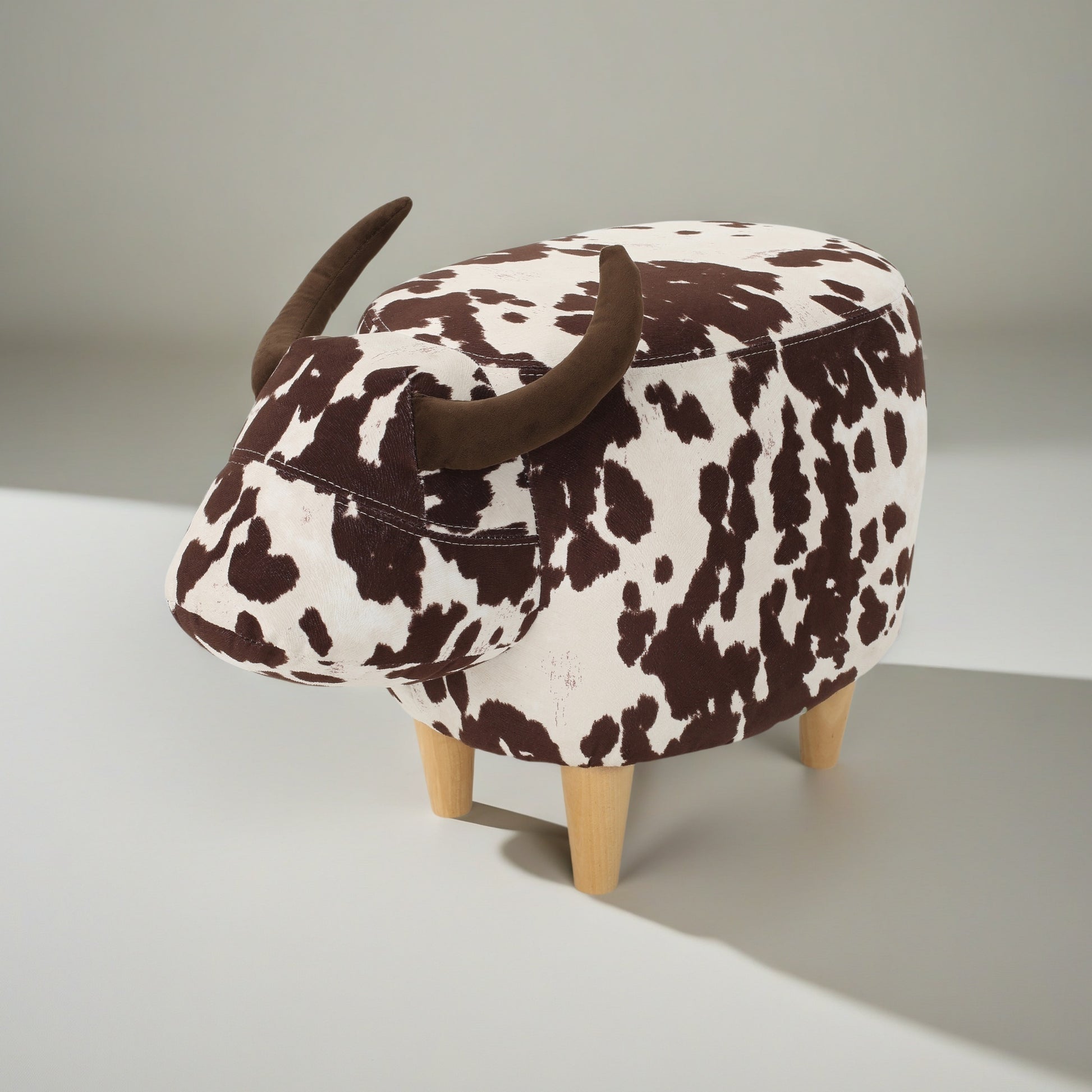 Brown and white cow print ottoman with fabric horns and wooden legs