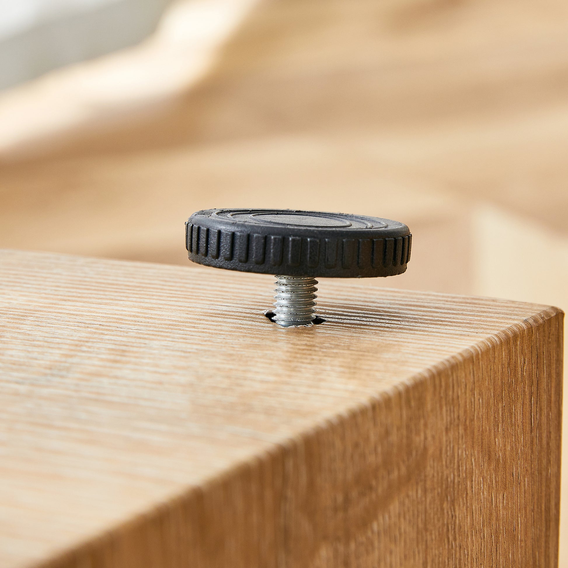 Black adjustable leveling foot with threaded bolt screwed into a wooden surface