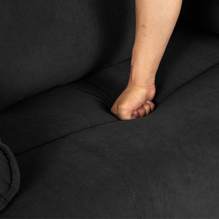 Closeup of a hand pressing into a plush black velvet couch cushion for comfort