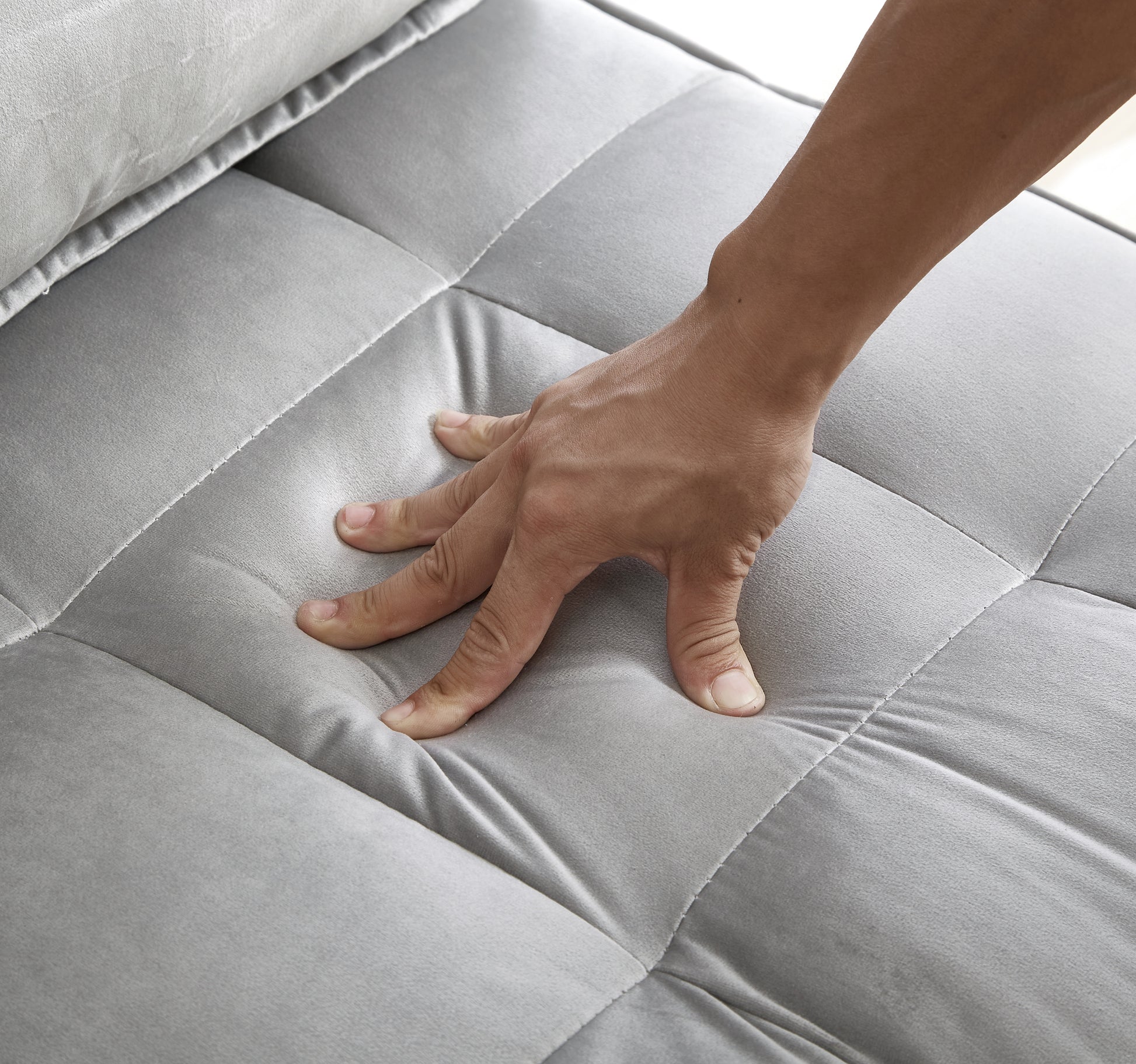 Closeup of a hand pressing into a plush grey velvet sofa cushion showcasing comfort