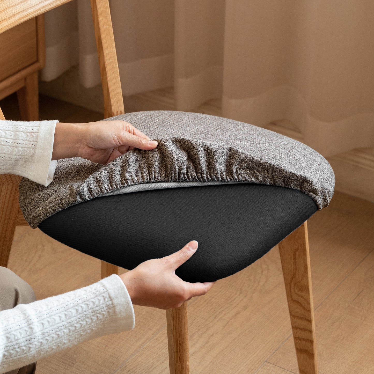Grey textured chair cover being fitted onto a black seat cushion for a modern dining chair