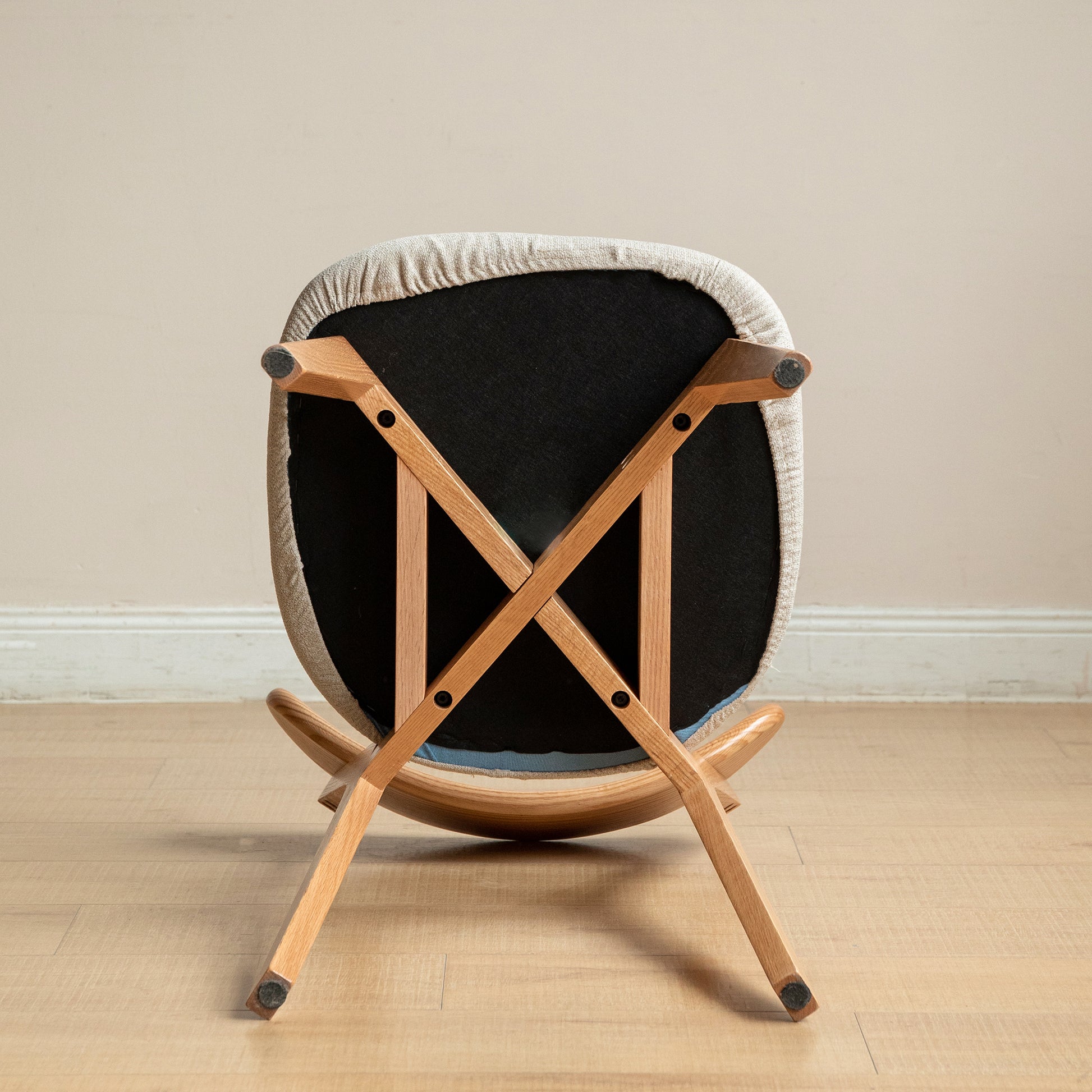 Underside view of a grey upholstered rocking chair with light wood legs