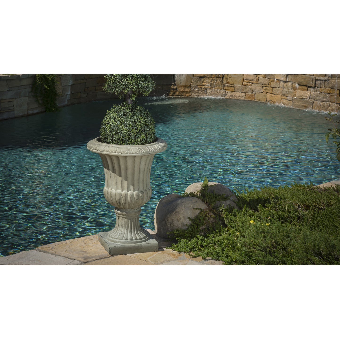 Cream urn planter with a sculpted boxwood topiary by a tranquil pool