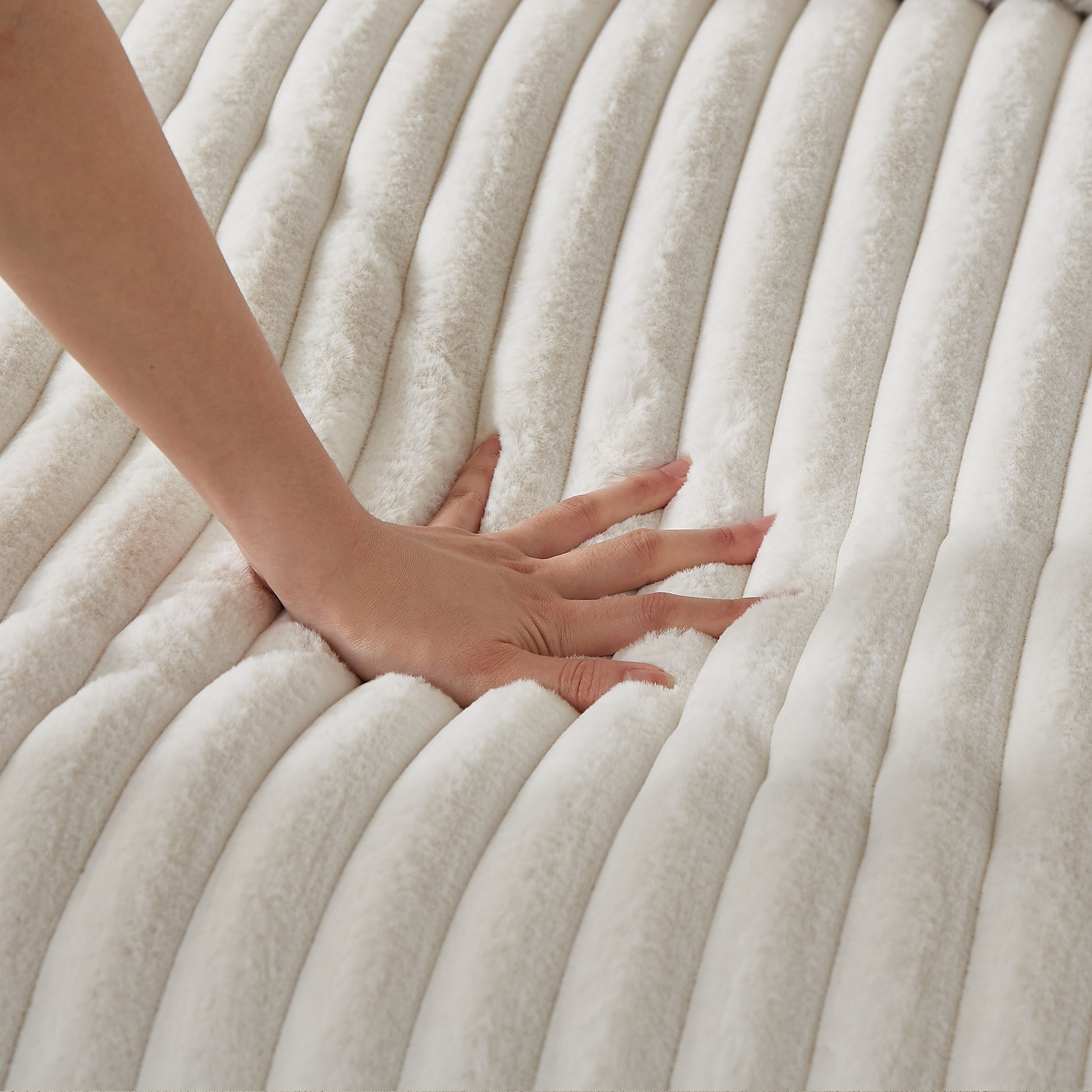 Closeup of a hand pressing into a plush creamcolored ribbed faux fur blanket showcasing its softness