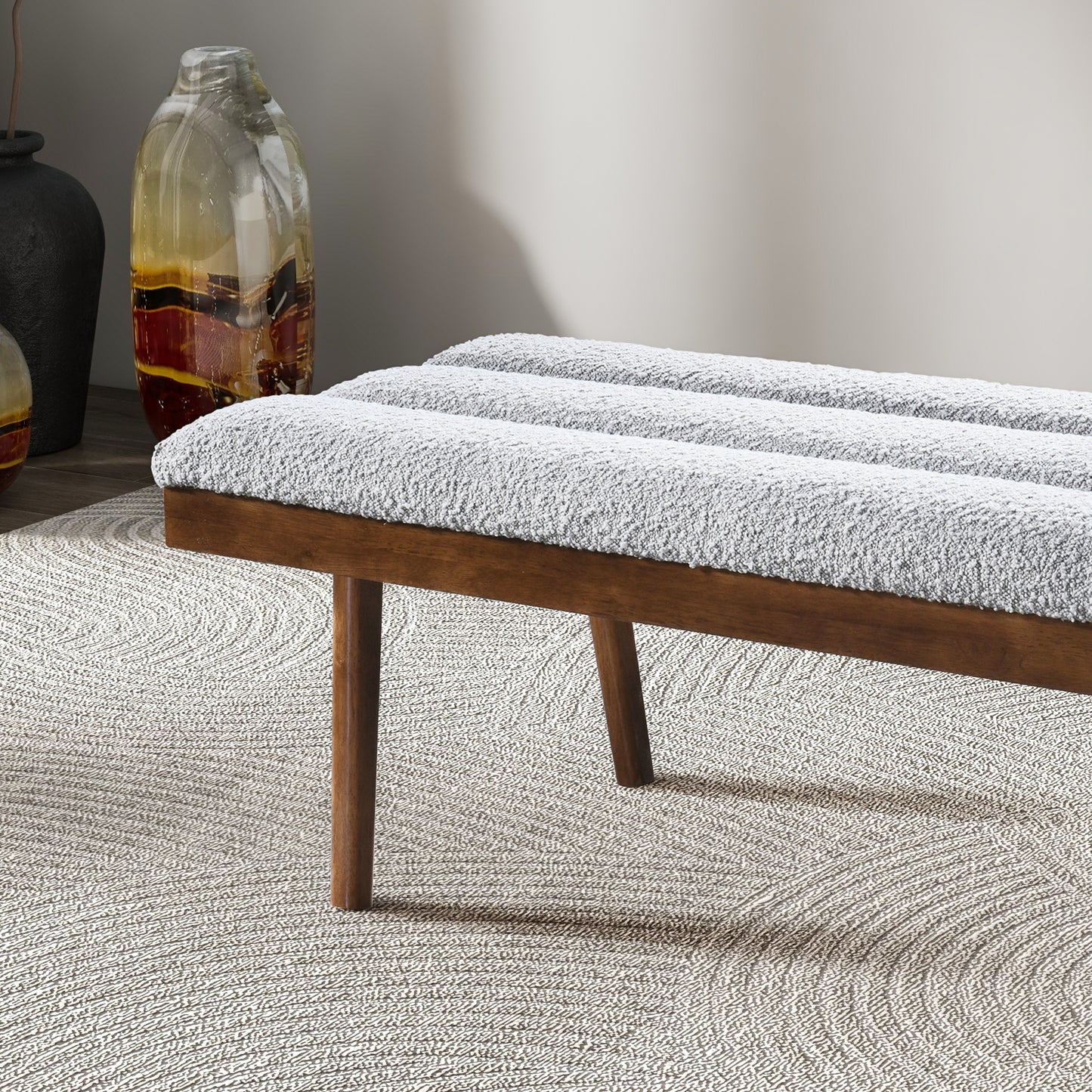 Gray boucle upholstered bench with wooden legs on a textured rug