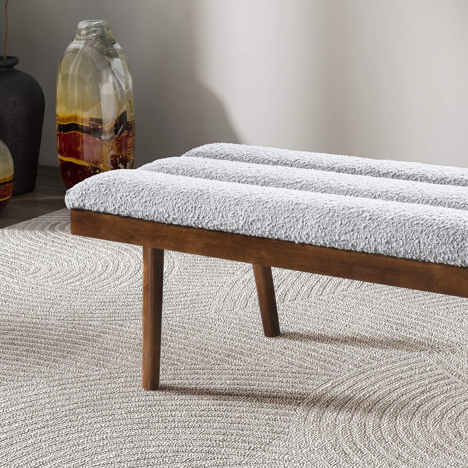 Gray boucle upholstered bench with wooden legs on a textured rug