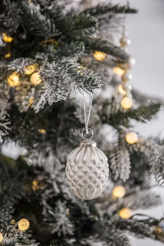 White textured pinecone Christmas ornament hanging on flocked tree