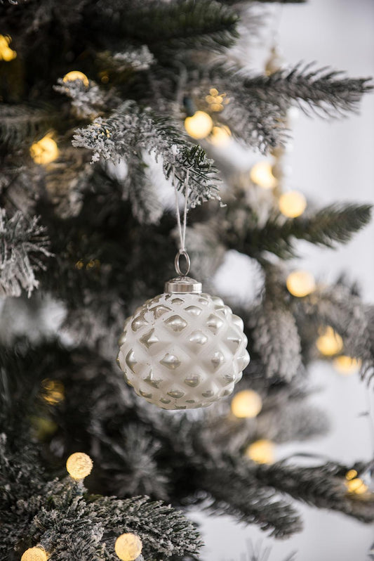 White diamondpatterned glass Christmas ornament hanging on frosted tree branch with bokeh lights