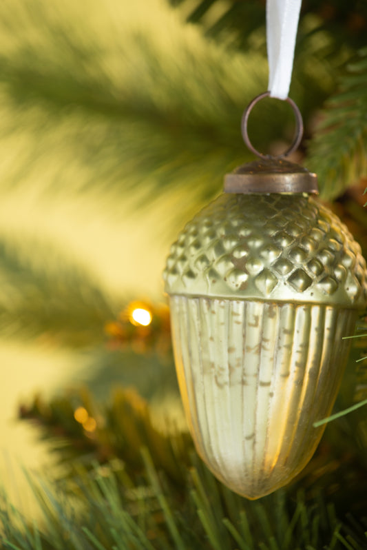 Gold acorn Christmas ornament with ribbed texture hanging on a tree